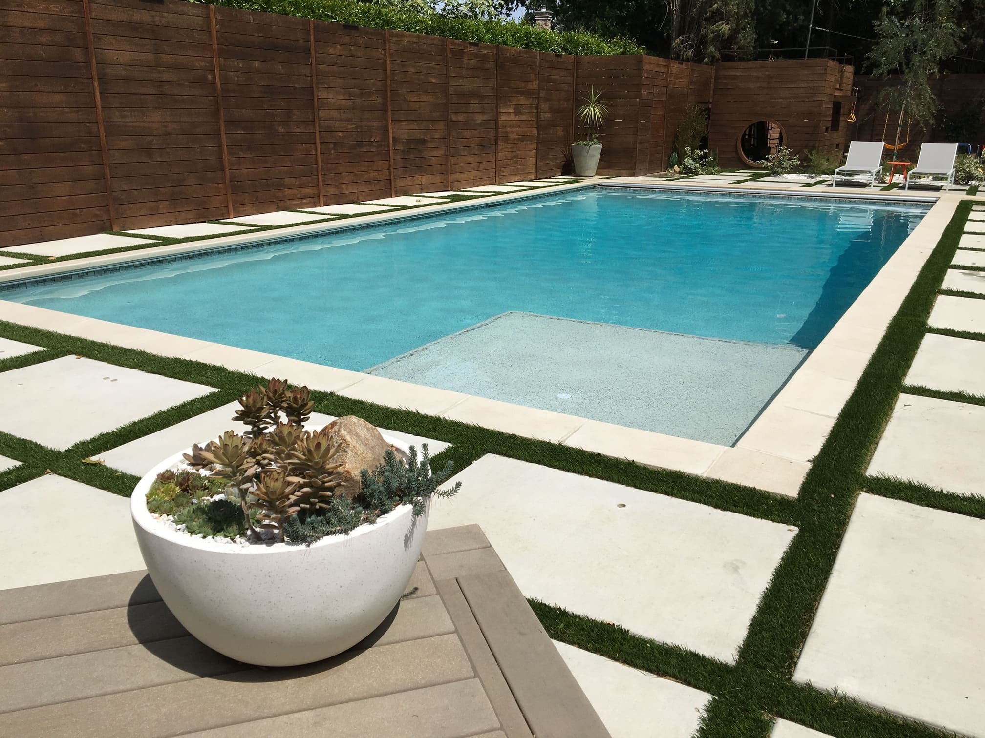 Modern backyard swimming pool with geometric turf decking and a white succulent planter