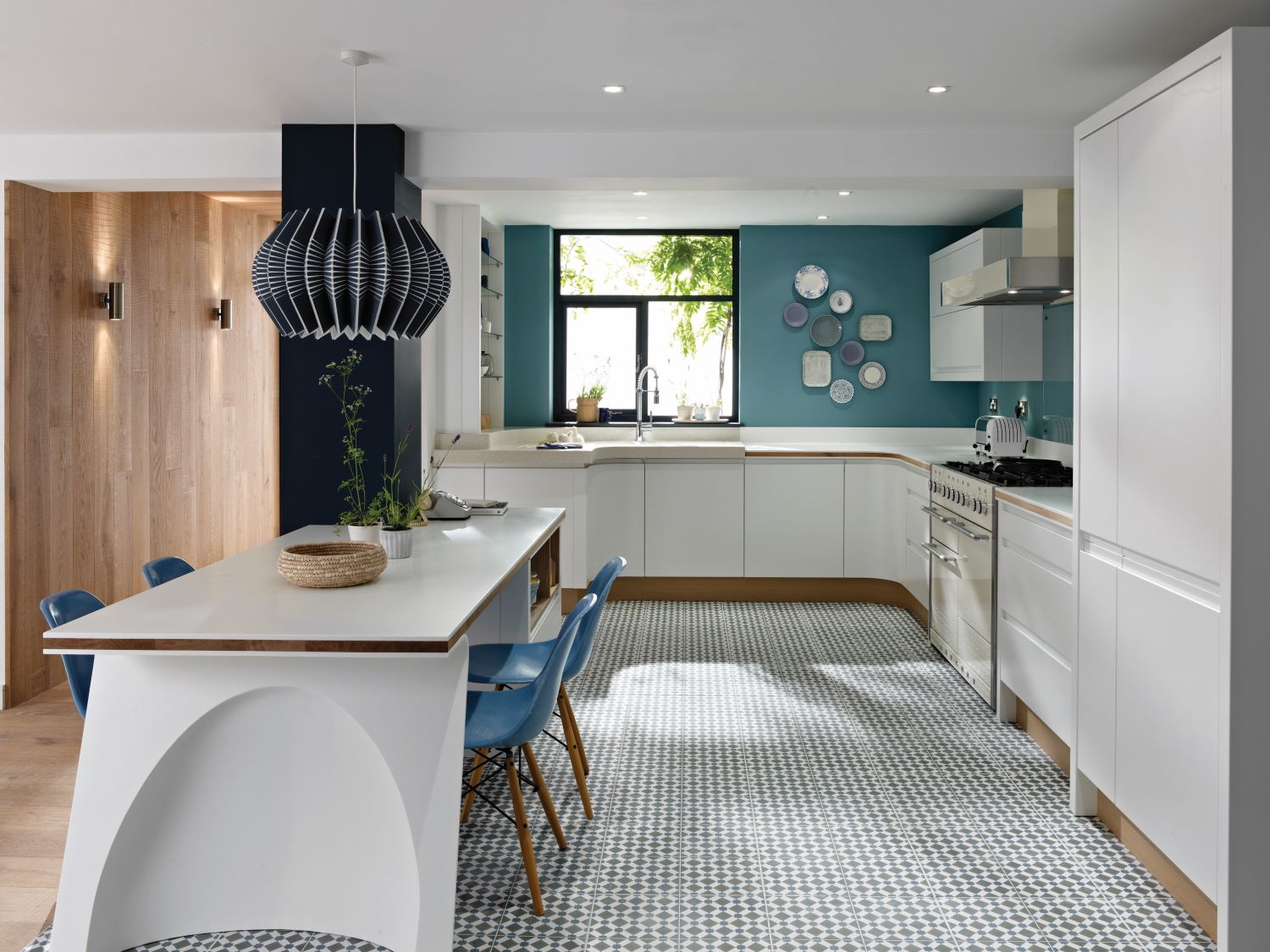 Modern kitchen with white cabinetry, blue accent wall, patterned floor tiles, and a white island with blue chairs and pendant light.