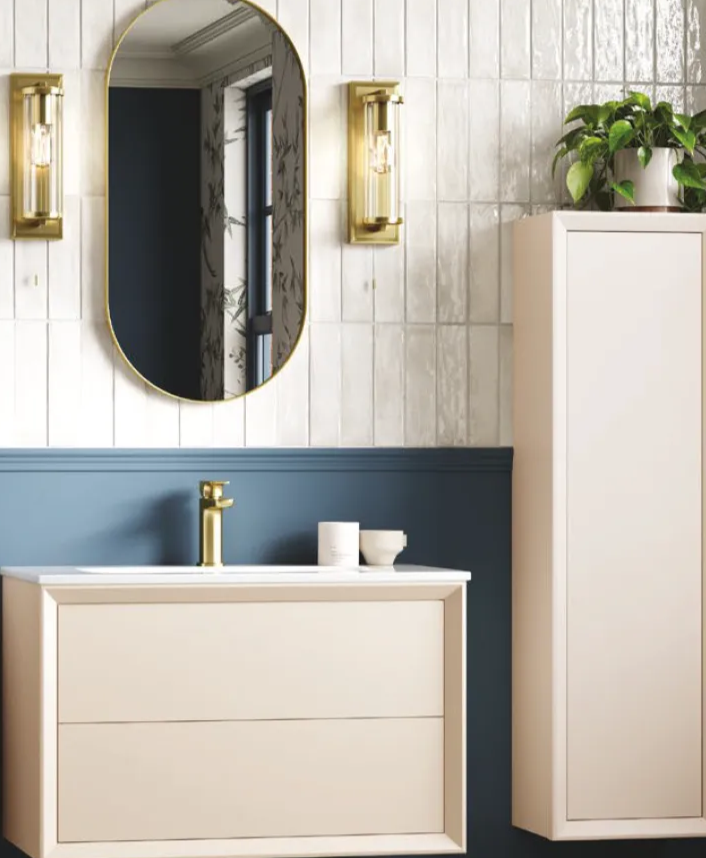 Modern bathroom vanity with gold faucet, oval mirror, wall sconces, and tall cabinet with potted plant on top.
