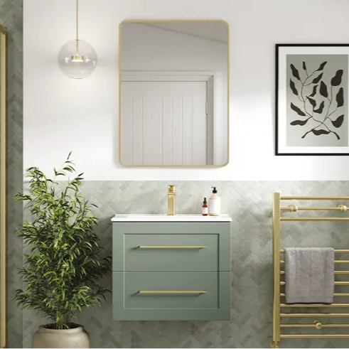 Modern bathroom with green floating vanity, gold faucet, a square mirror, potted plant, gold towel rack with gray towel, and framed abstract leaf artwork.