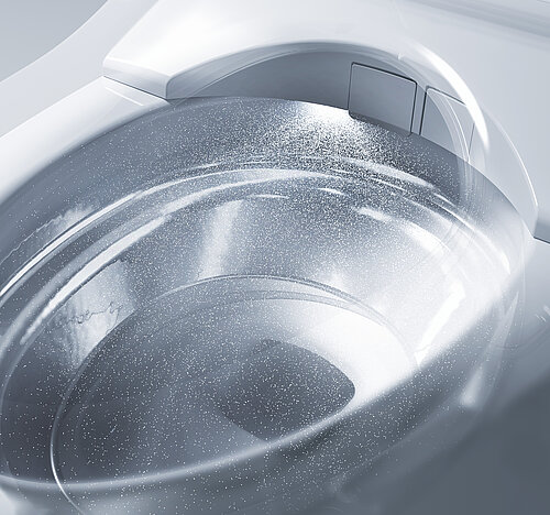 Close-up of a sleek, modern washing machine drum with mist and water droplets inside.