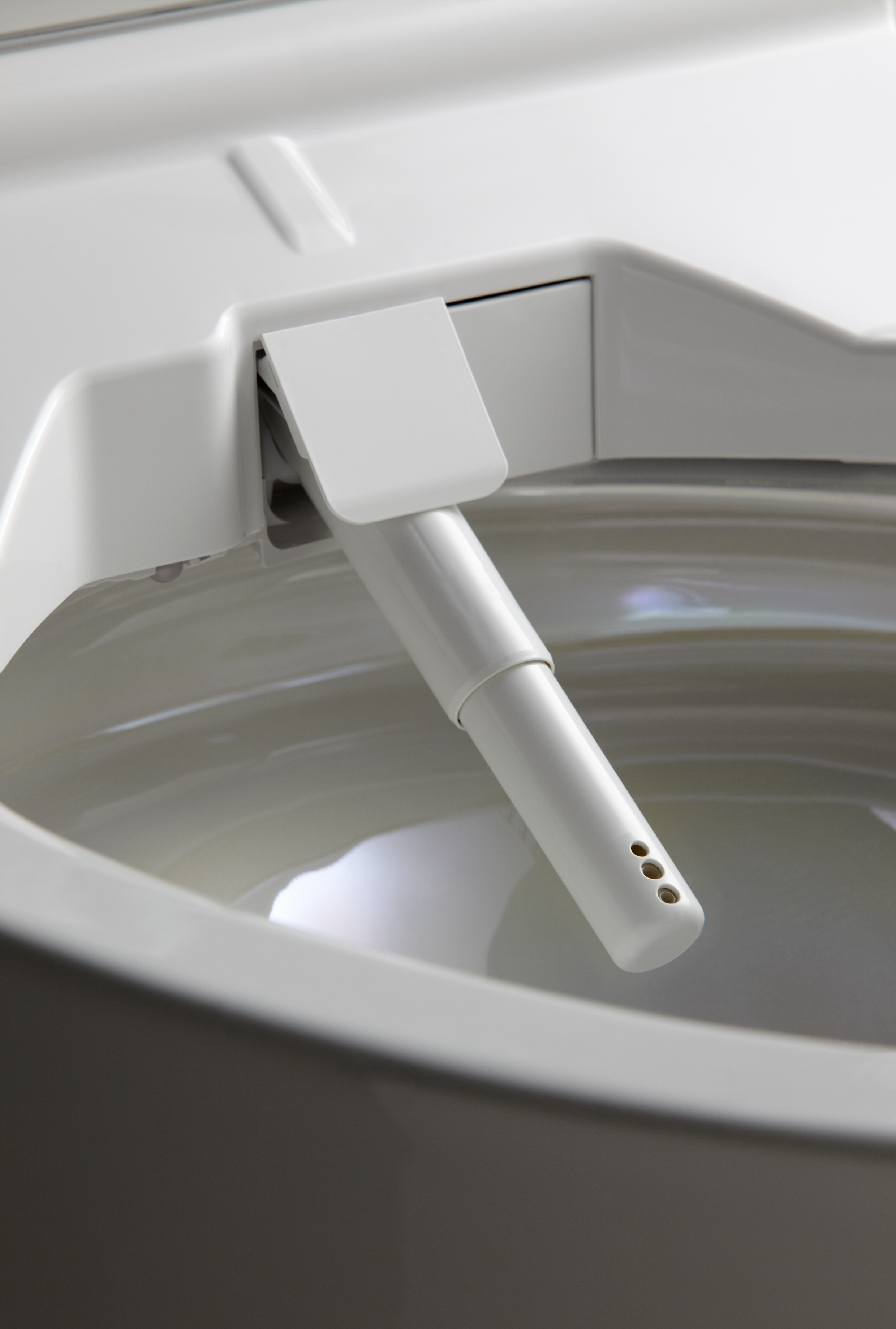 Close-up of a white bidet nozzle extending inside a toilet bowl.