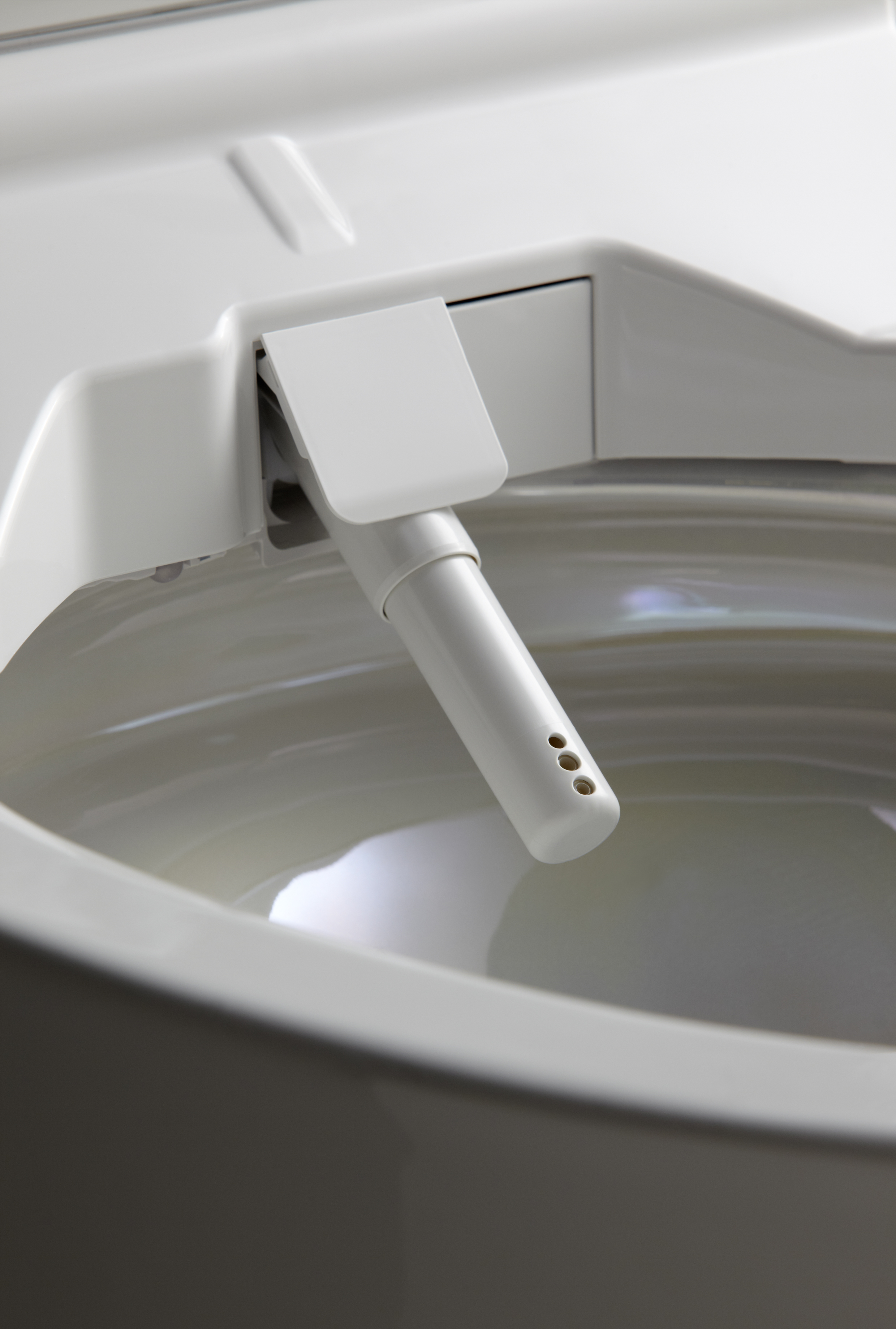 Close-up of a white bidet spray nozzle inside a toilet bowl.