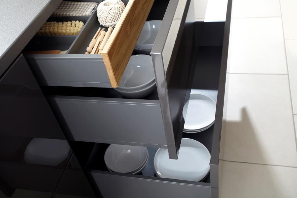 Open kitchen drawers revealing organized wooden utensil tray, dish brush, and stacked white ceramic plates.