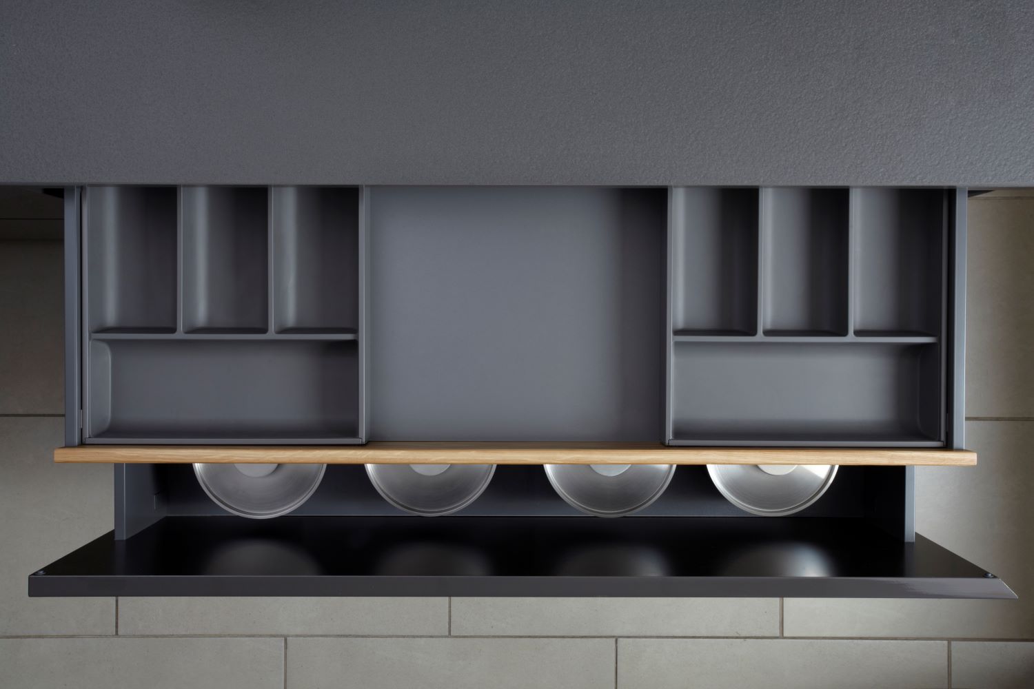 Top-down view of an open drawer with organized compartments and four metal bowls underneath.