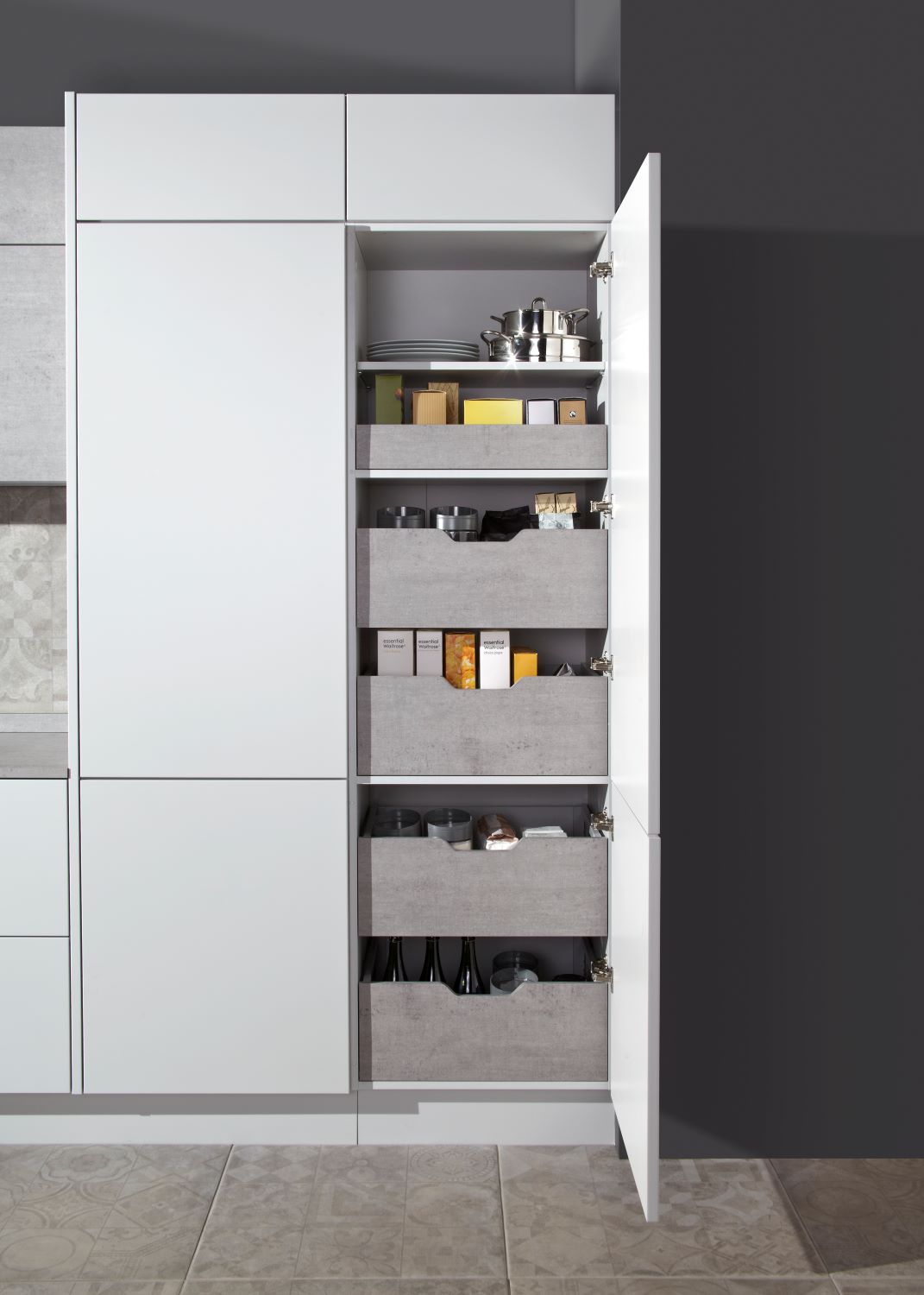 Modern kitchen pantry with white door open revealing shelves and drawers holding pots, plates, various food items, and bottles.