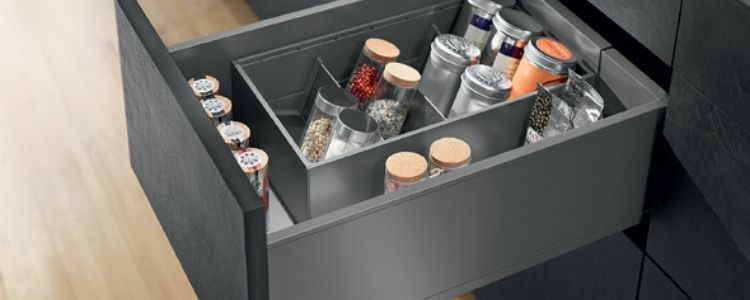 Open kitchen drawer organized with various jars and containers holding spices and dry ingredients.