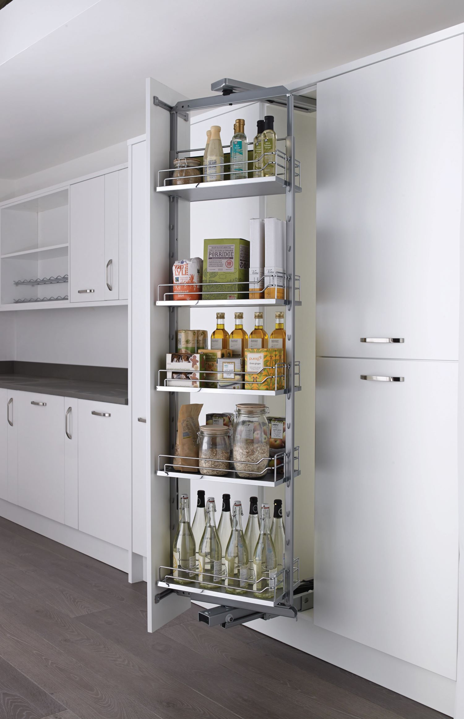 Pull-out pantry cabinet with five shelves holding bottles, jars, and boxed food items in a modern white kitchen.