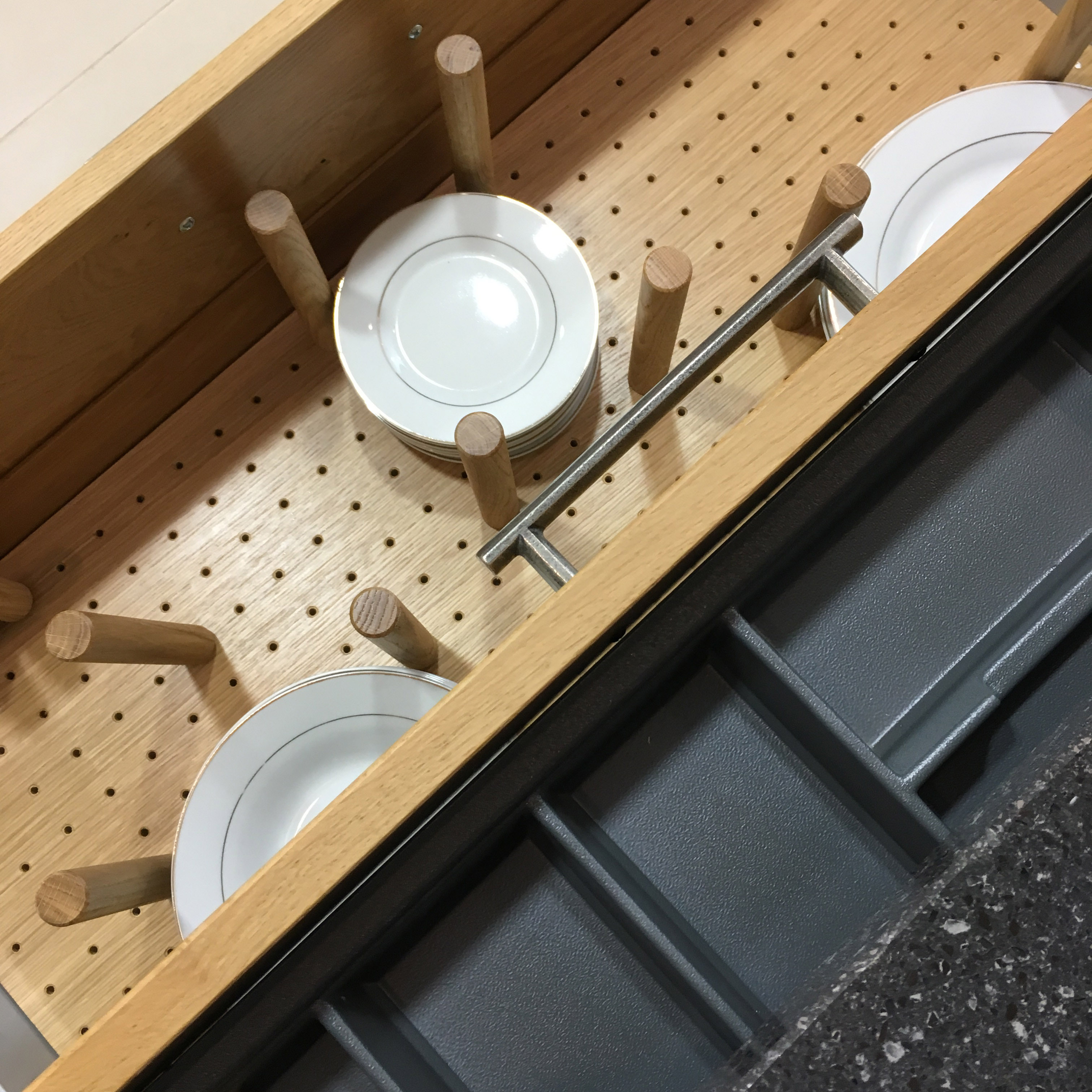 Wooden drawer organizer with wooden pegs holding stacked white plates with silver rims.