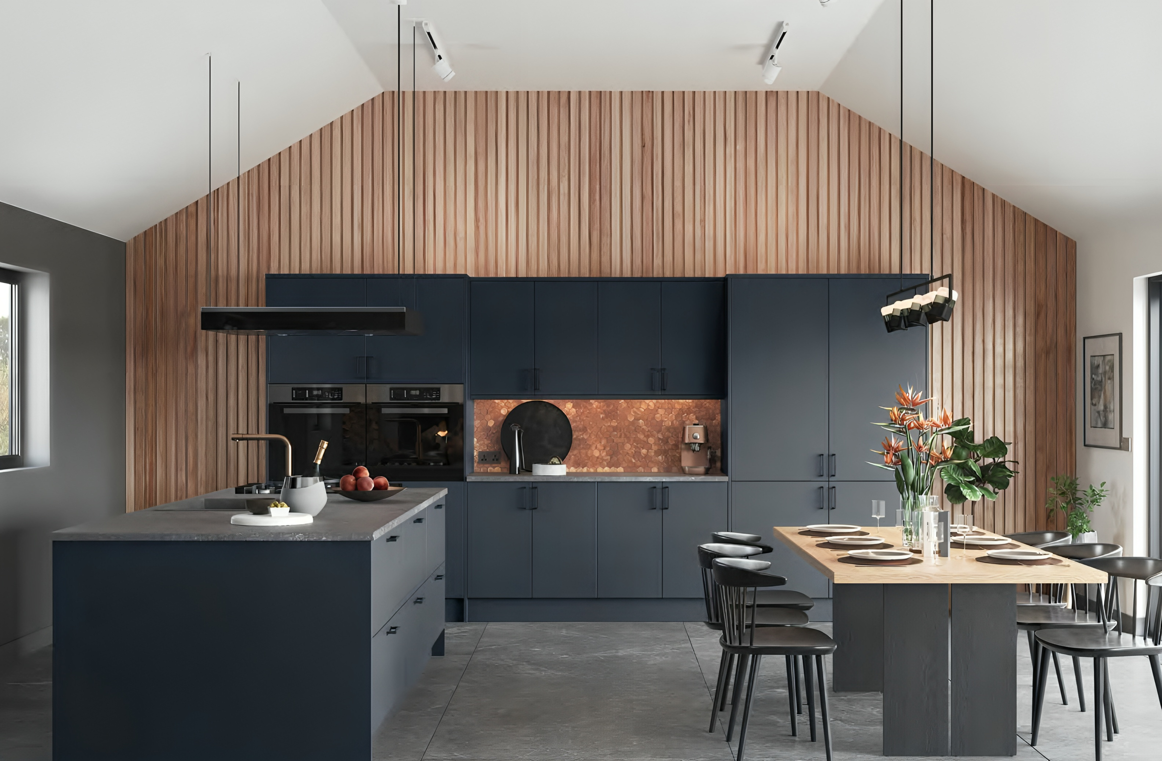 Modern kitchen with dark blue cabinets, wooden slat wall, kitchen island, and dining table with black chairs and orange flowers.
