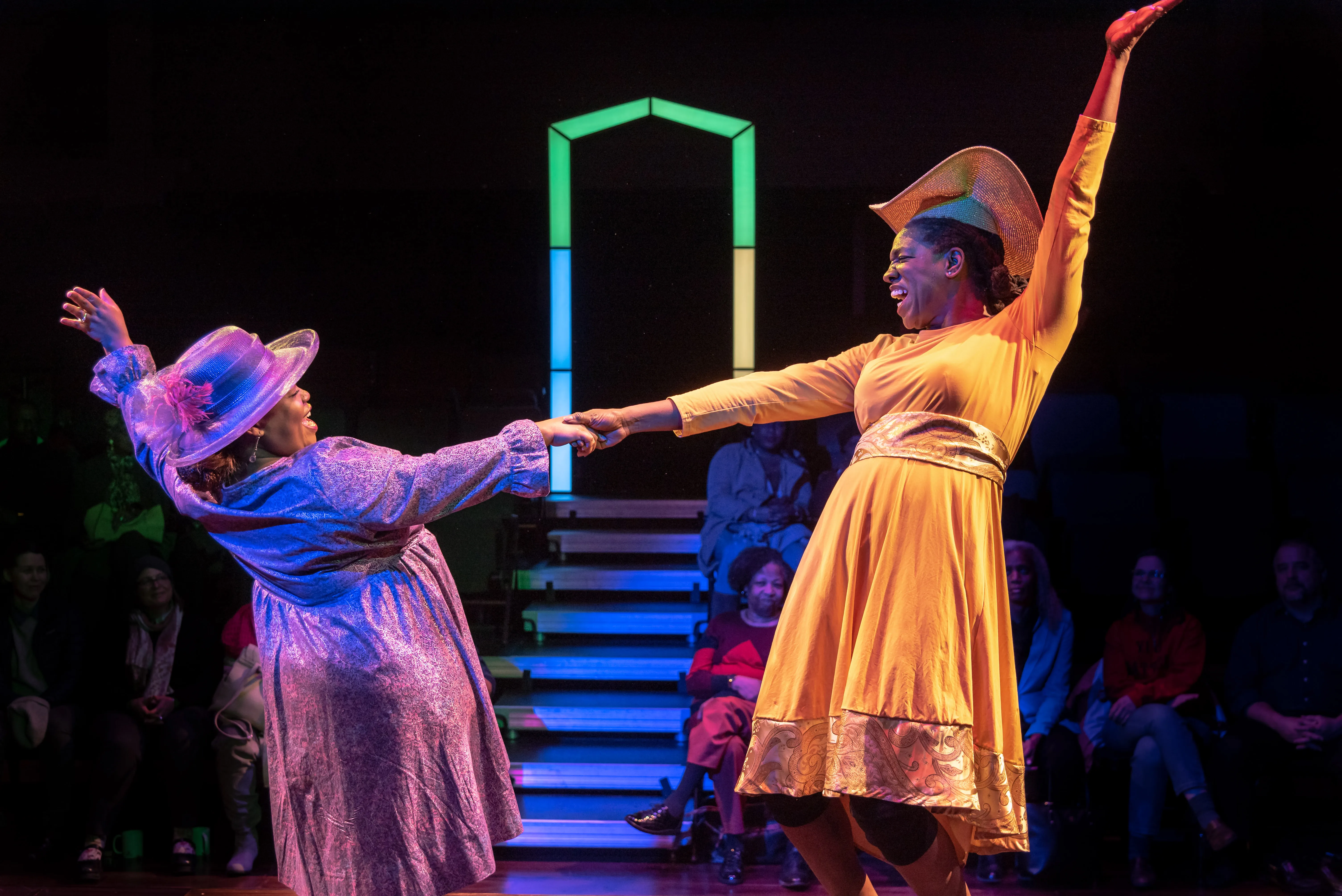 2 women in dresses with matching hats, dancing on a stage