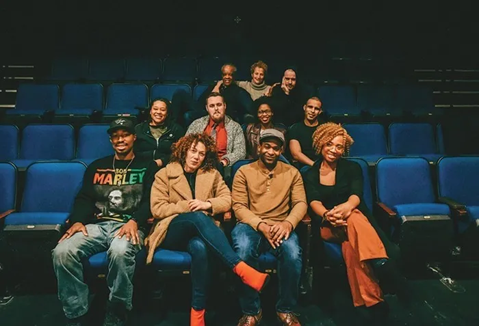 A group of actors and writers sitting in blue theater seats