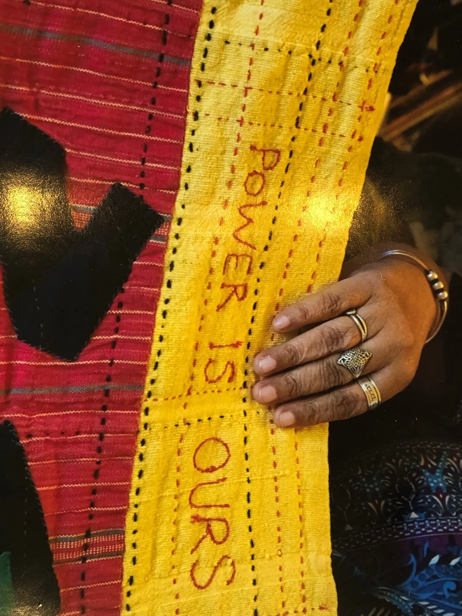 Red and yellow hand-stitched quilt held by a hand with rings on it. Photo Credit Intisar Abioto.