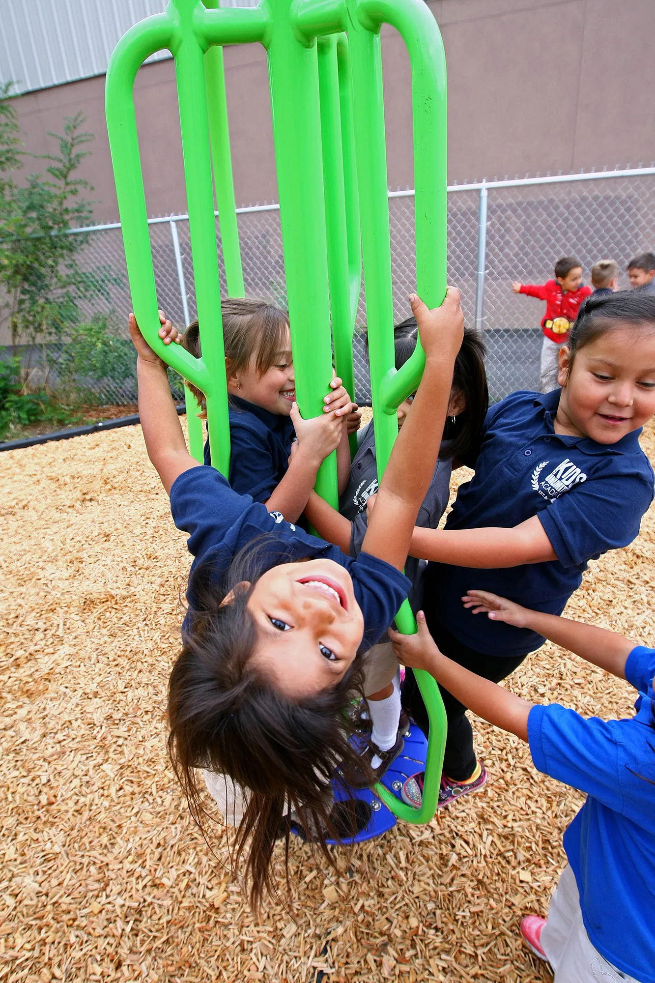 Four 5 to 6 year old students in matching blue polo shirts playing on  green and blue playground equipment; Photo courtesy of Kids Unlimited of Oregon