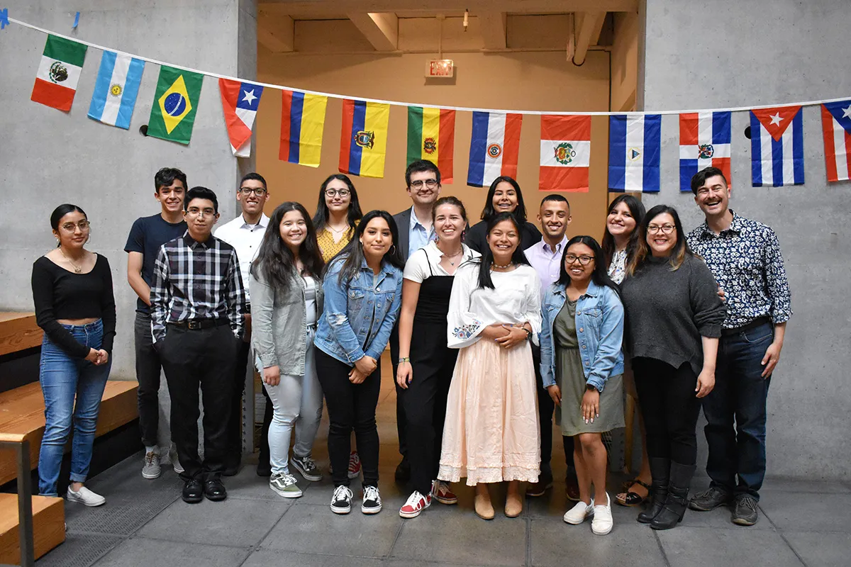 14 high school students standing with 2 adult leaders. Latin American flags in the background.