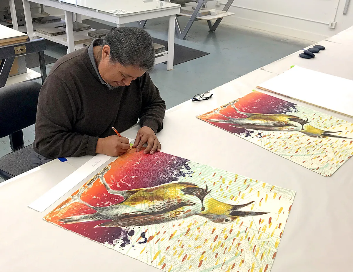 Visual artist, seated, working on a print of a bird