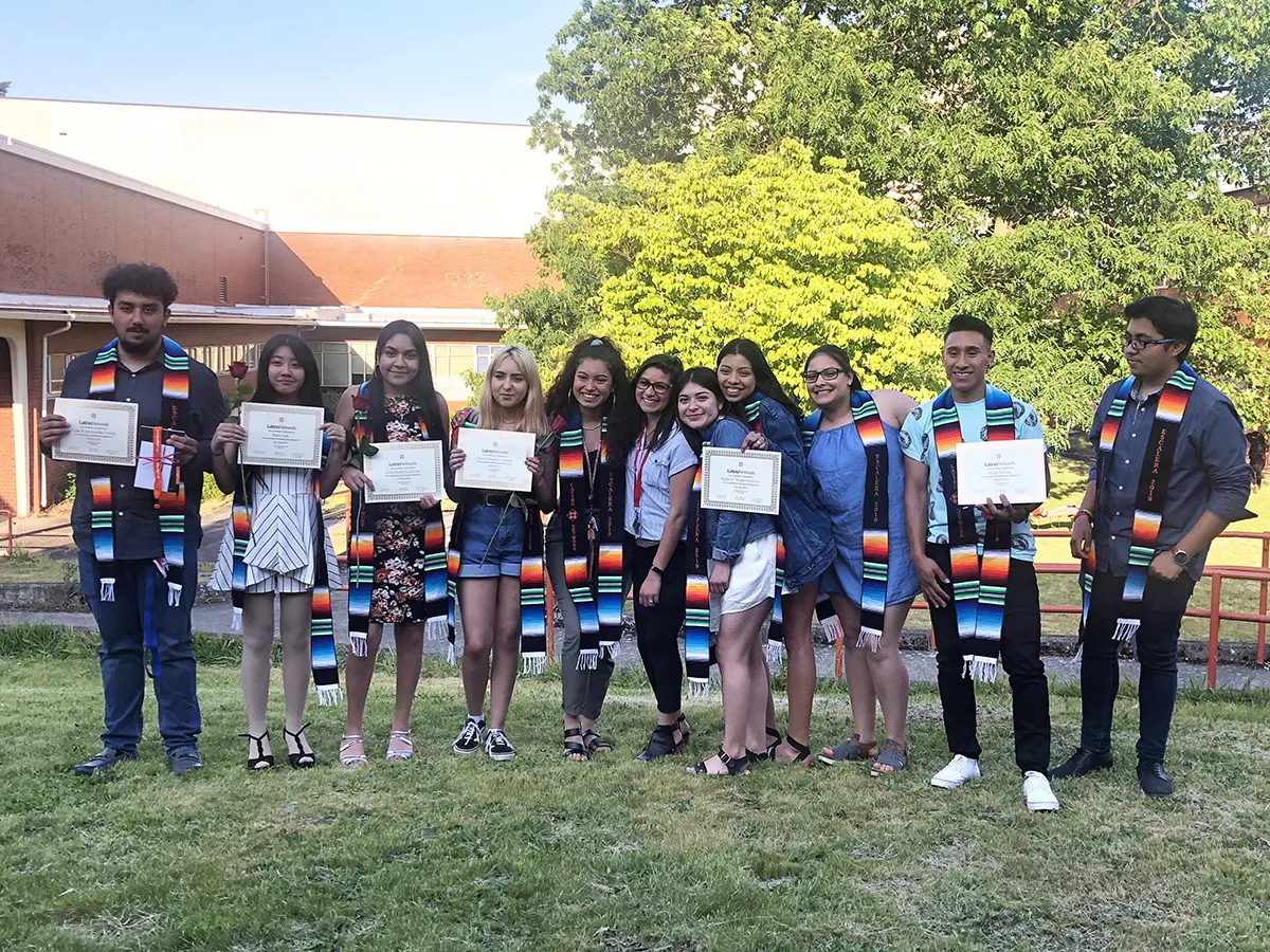 A group of high school students standing on a lawn outside, holding diplomas