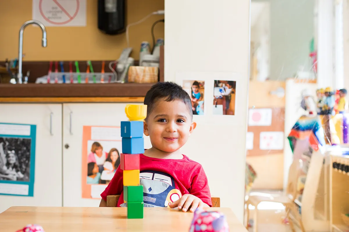 A young child, sitting in a preK classroom in front of a stack of blocks