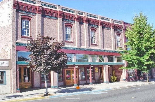 Exterior of the Historic G Street building houing Grants Pass Museum of Art, a two story brick building with storefronts opening onto a sidewalk with trees