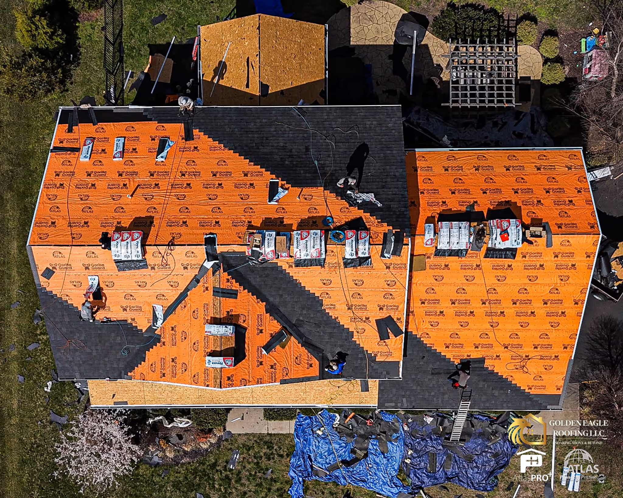 Aerial view of workers installing roofing shingles on a house with orange underlayment