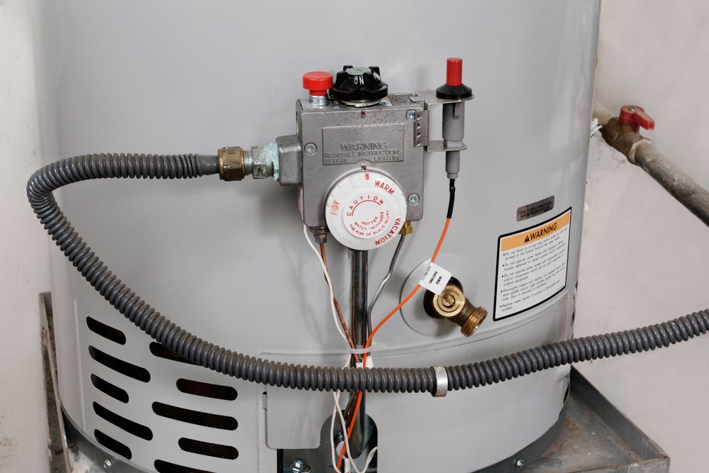 Close-up of a gray residential hot water tank with temperature control dial and warning label.