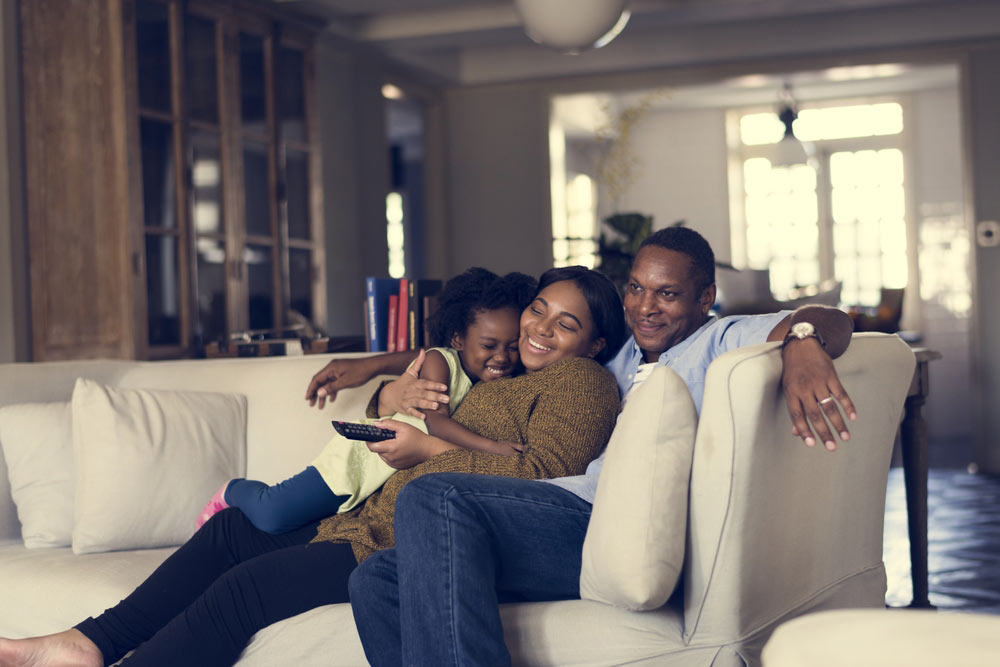 A happy family of three cuddling and relaxing on a beige couch in a cozy living room.
