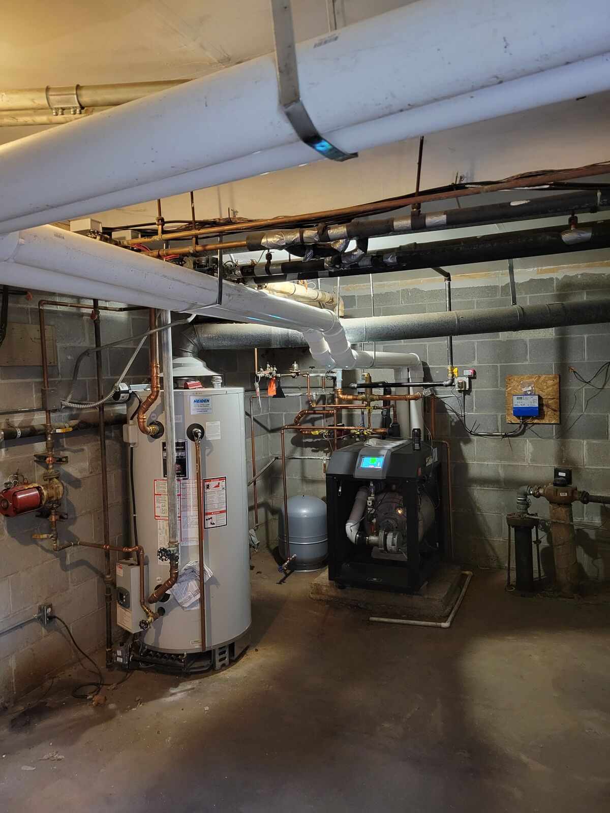 Basement utility room with water heater, boiler, and various copper and insulated pipes attached to concrete block walls.