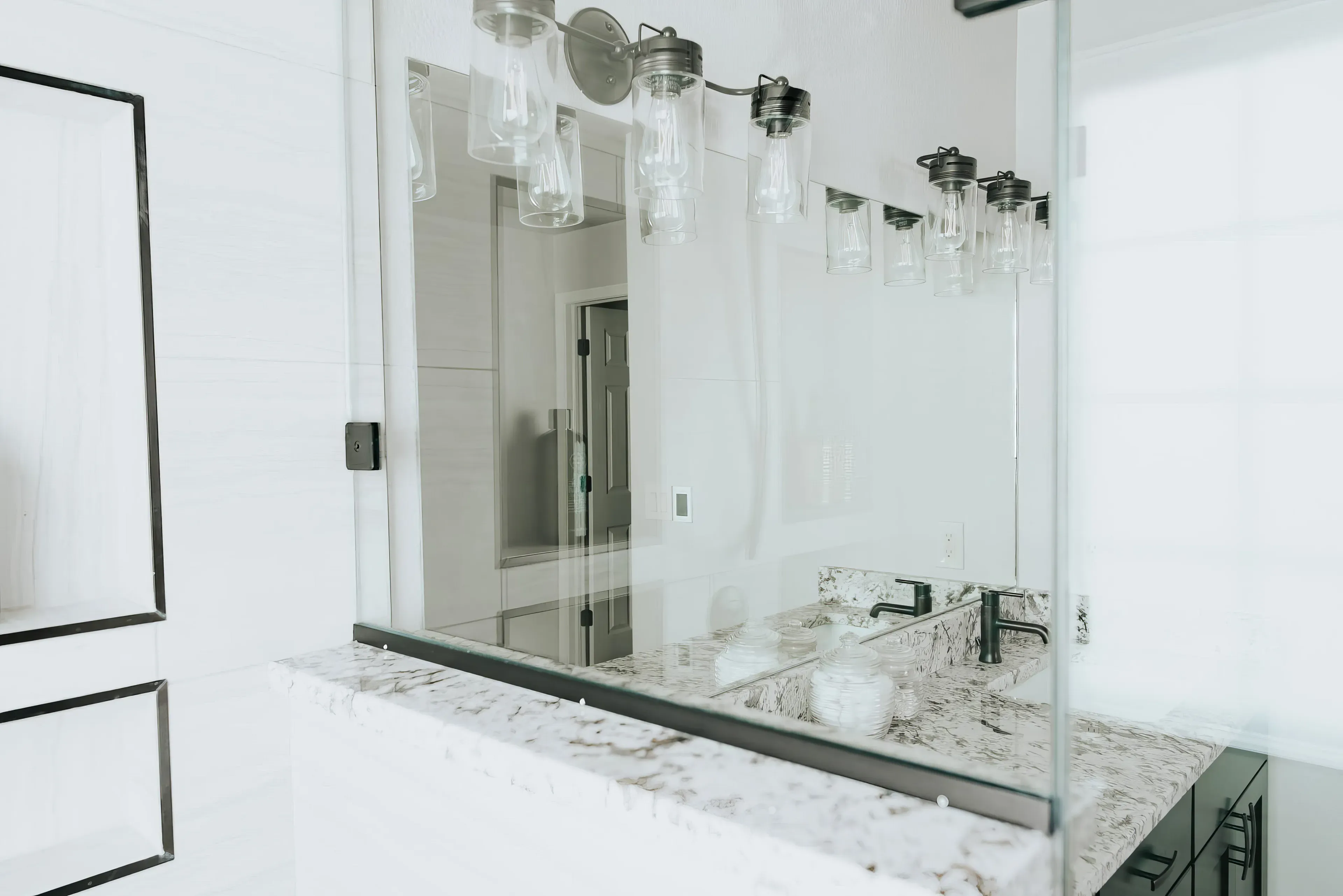 A photograph of a new remodeled bathroom with a walk-in shower, small sauna with a white and black marble counter top and custom light fixtures
