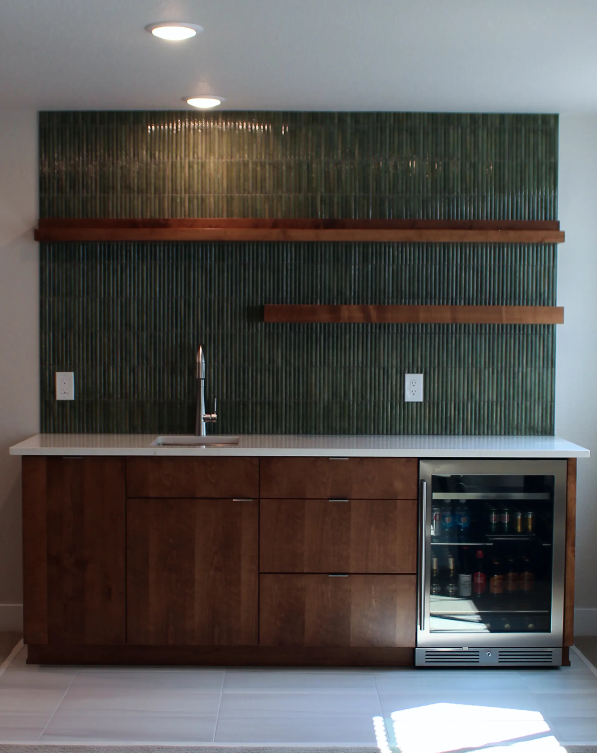 Full view of finished wet bar with floating shelves, contemporary faucet, and moody green tile for contrast.