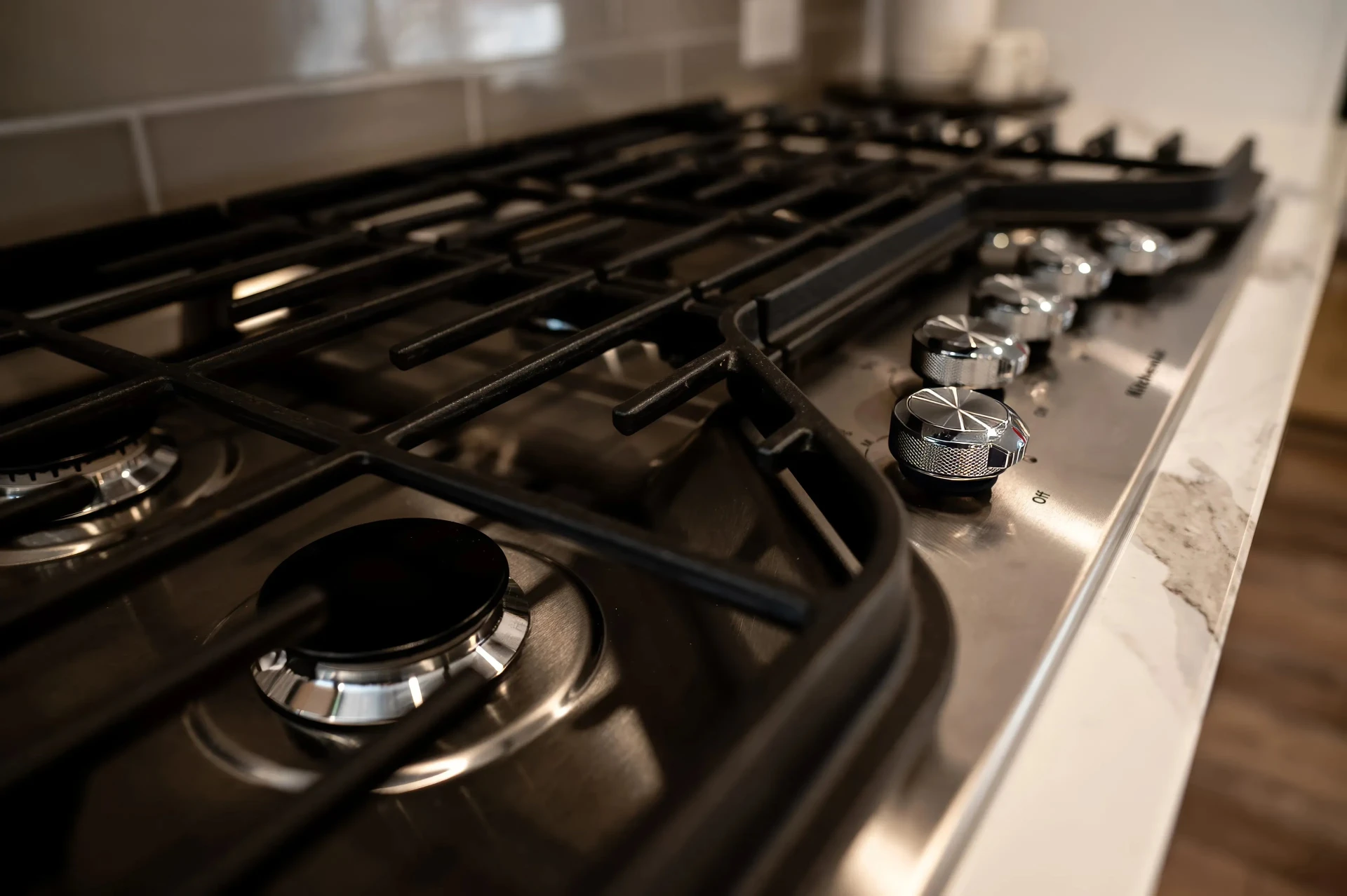Close-up of a modern stainless steel gas stove with black grates and shiny silver knobs, set in a sleek kitchen environment, conveying elegance.