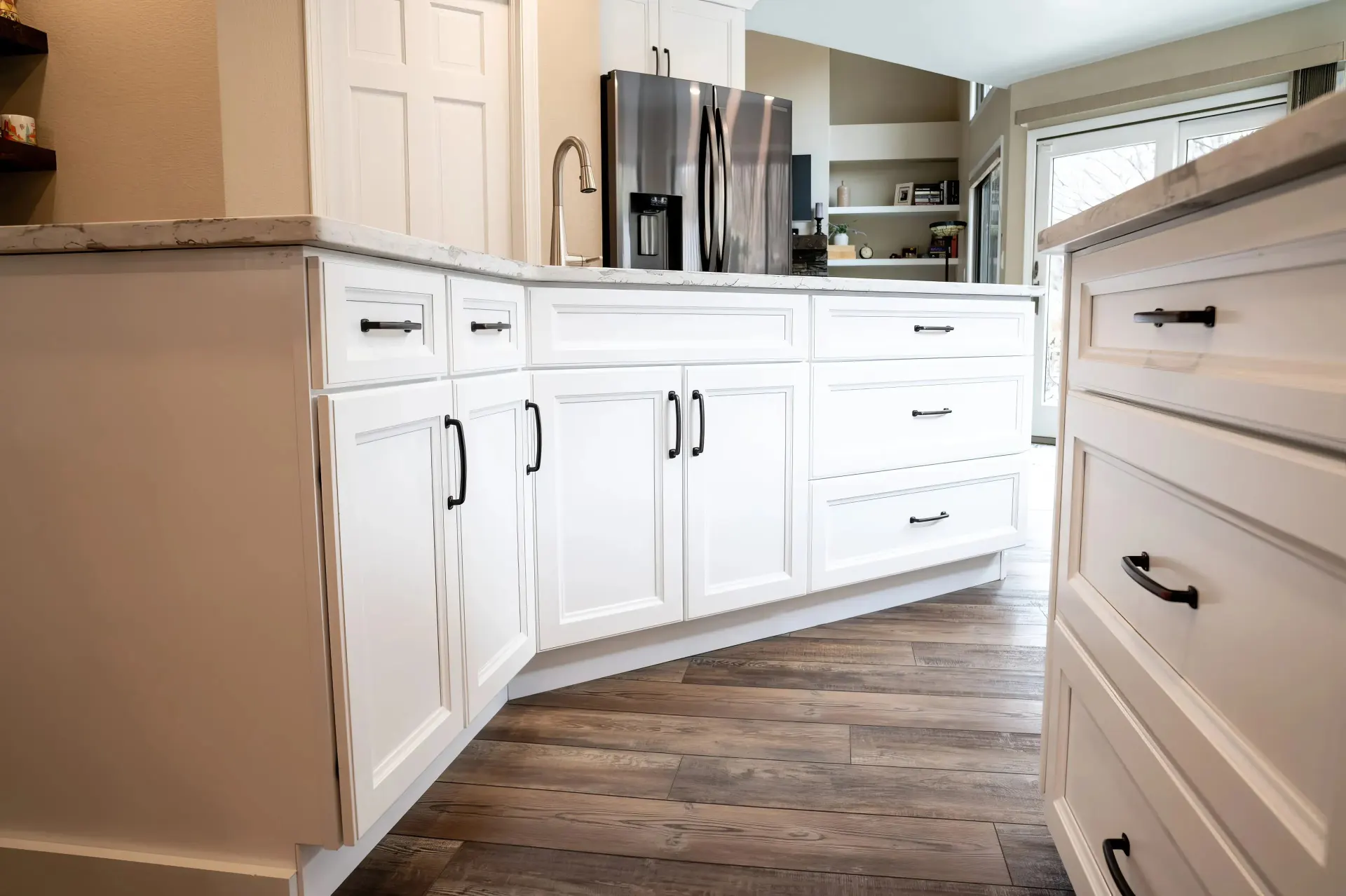 Bright kitchen with white cabinets and black handles, wood floor, stainless steel fridge, and modern sink, creating a clean, inviting atmosphere.