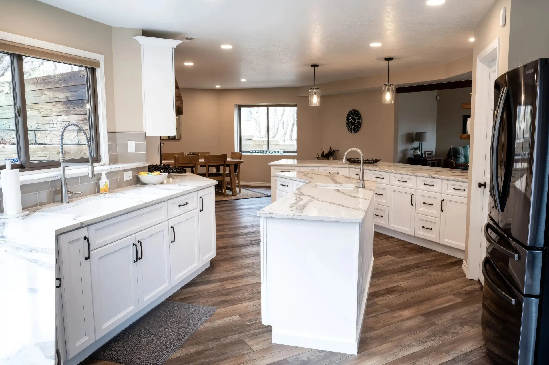 Spacious kitchen with white cabinets and marble countertops. Features a central island, modern fixtures, and wood flooring. A dining area is visible in the background, providing a warm, inviting atmosphere.