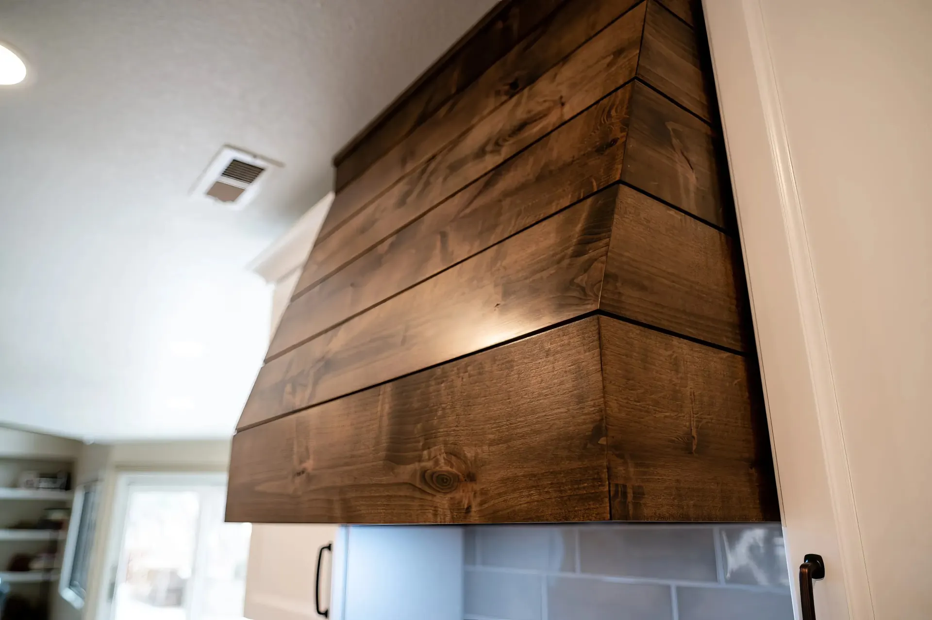 Modern kitchen featuring a dark wood range hood with a sleek finish. The room is bright, showcasing a cozy, inviting atmosphere with natural light.