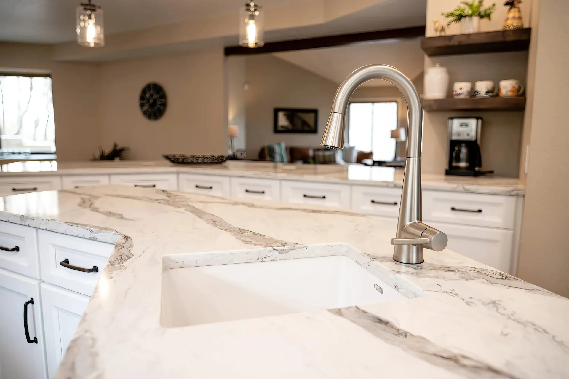 Modern kitchen with white marble countertops featuring gray veins, a sleek silver faucet, white cabinets with black handles, and cozy ambient lighting.