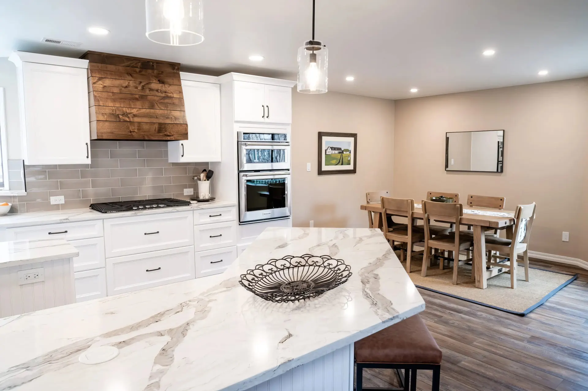 Spacious kitchen with white cabinets, marble island, and wooden accents. Dining area with rustic table, neutral tones, and a warm, inviting ambiance.