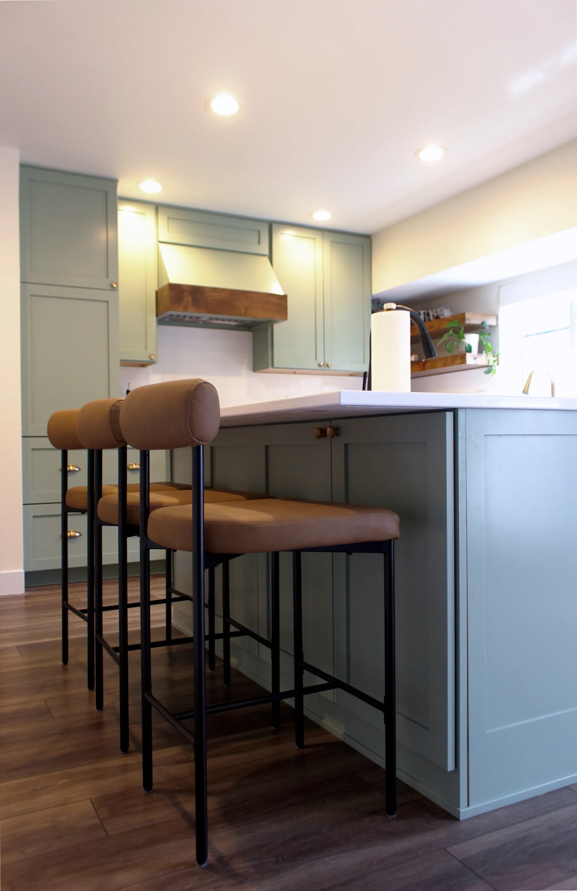 A photograph of modern barstools at a green kitchen island with white marble countertops.