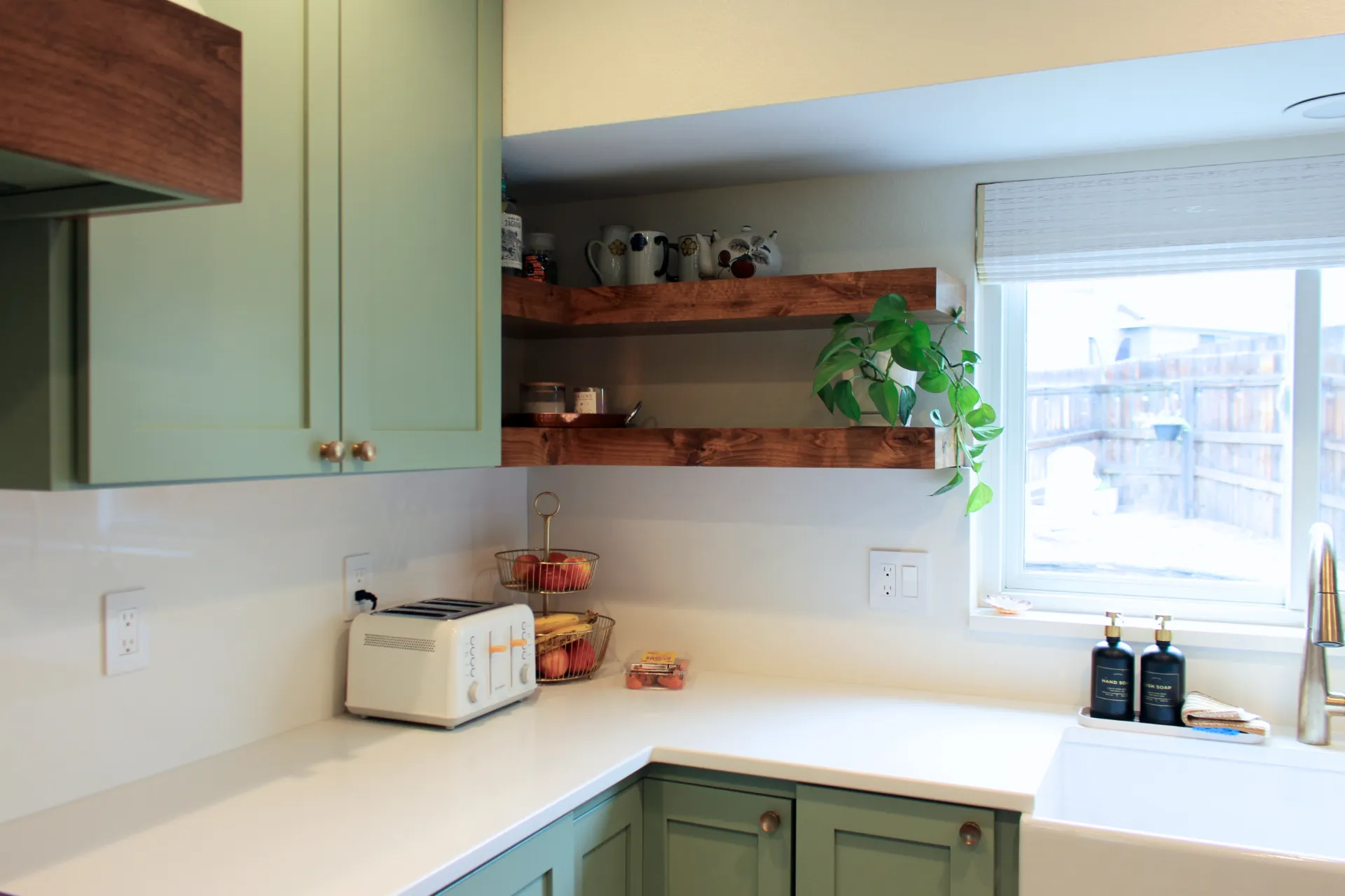 A close up photograph of custom floating shelves with decorative jars and a houseplant, and white marble kitchen counters.