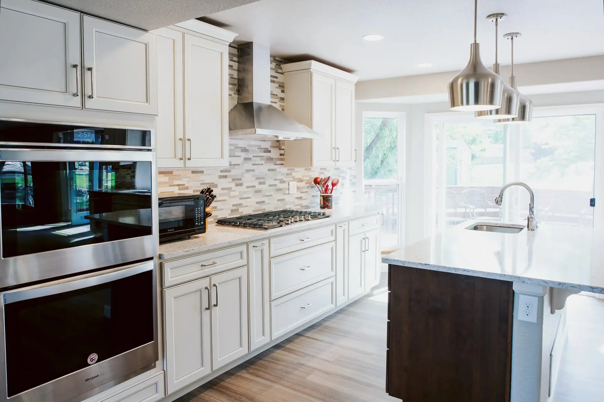 A photograph of a bright kitchen with a double oven, stainless range hood, and kitchen island.
