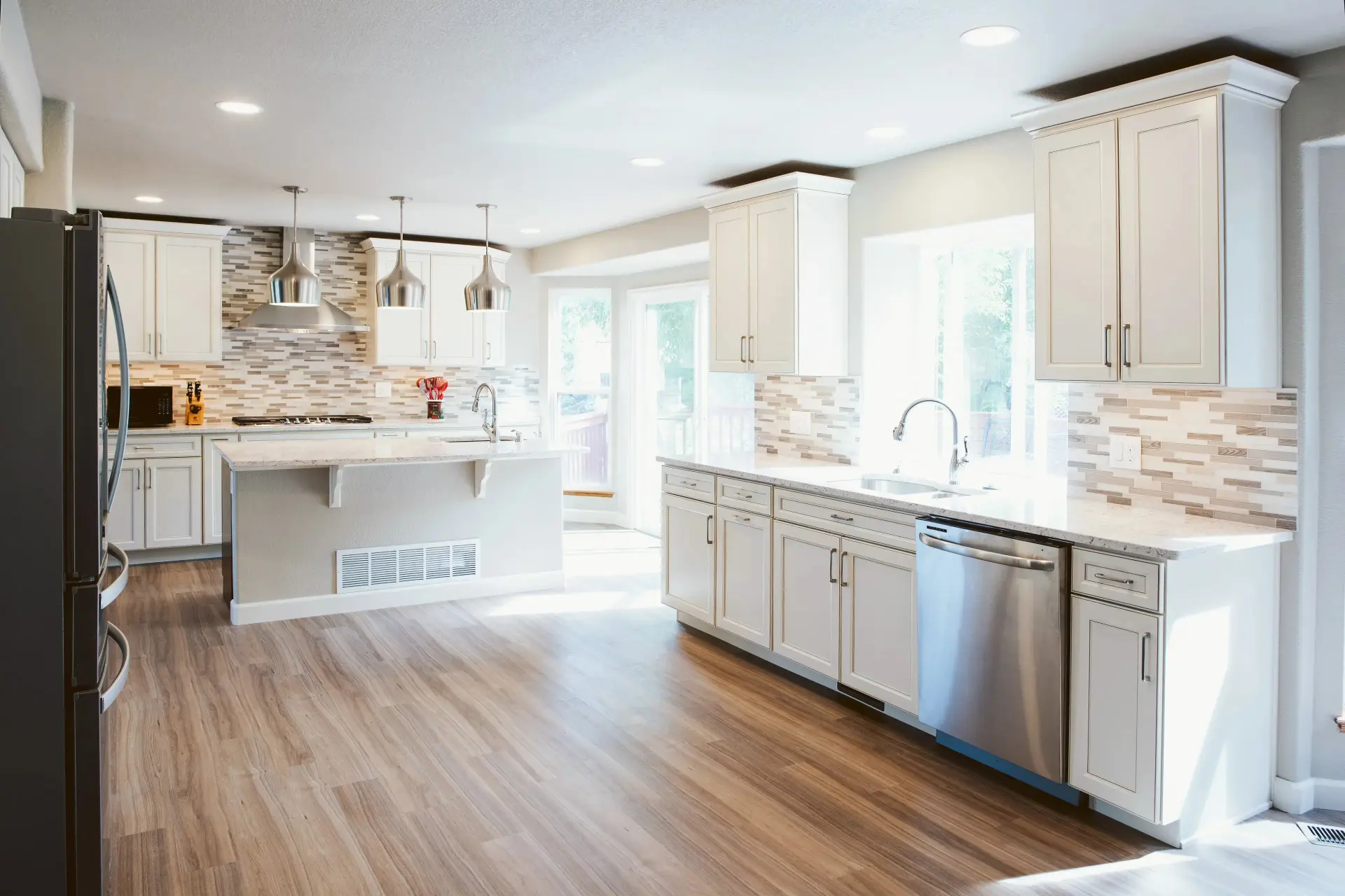 A wide view of a custom kitchen with white cabinets, countertops, and light brown luxury vinyl plank flooring.