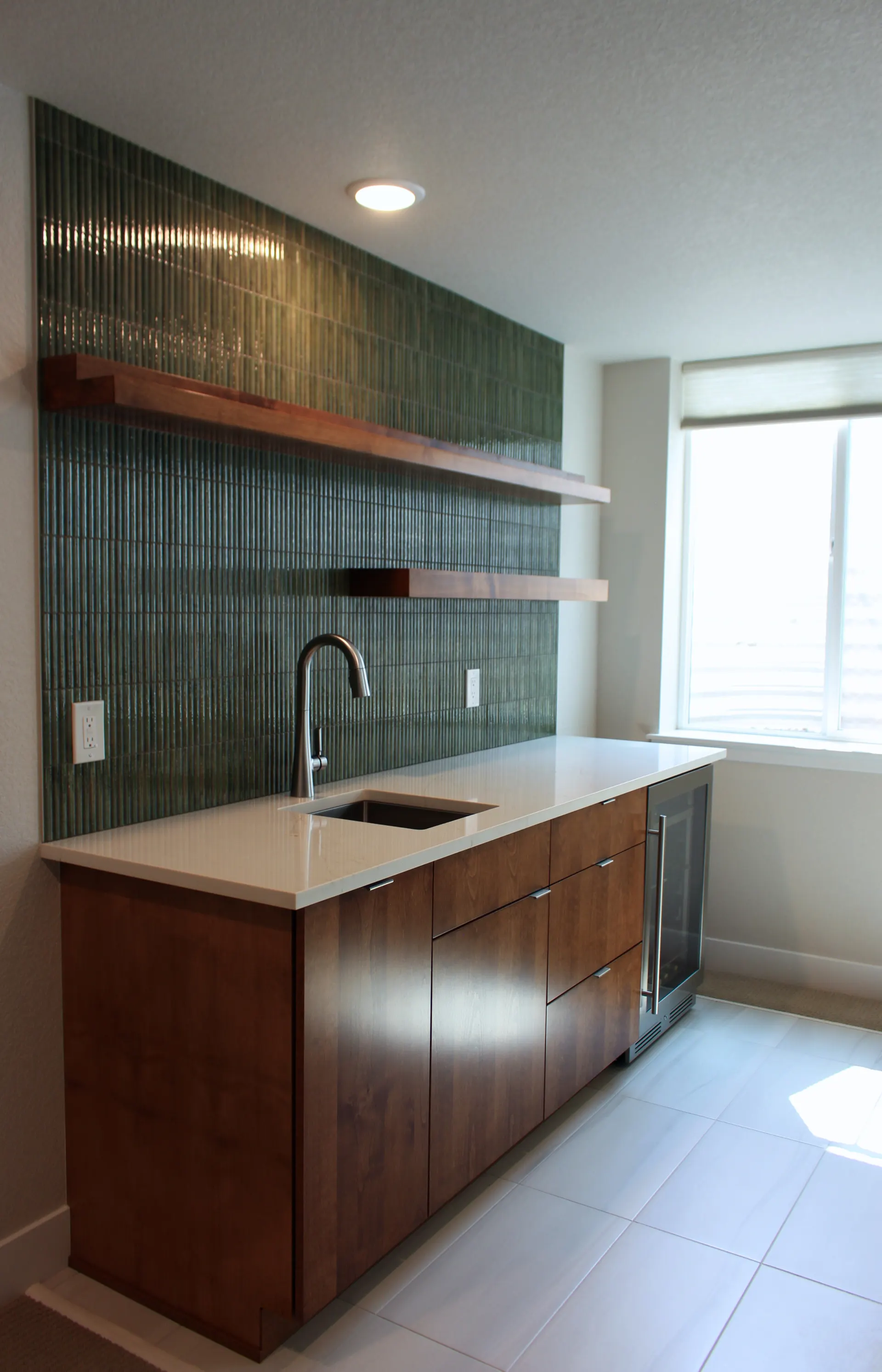 Side angle of wet bar featuring minimalist faucet, clean white counter, and mid-century style wood cabinetry.