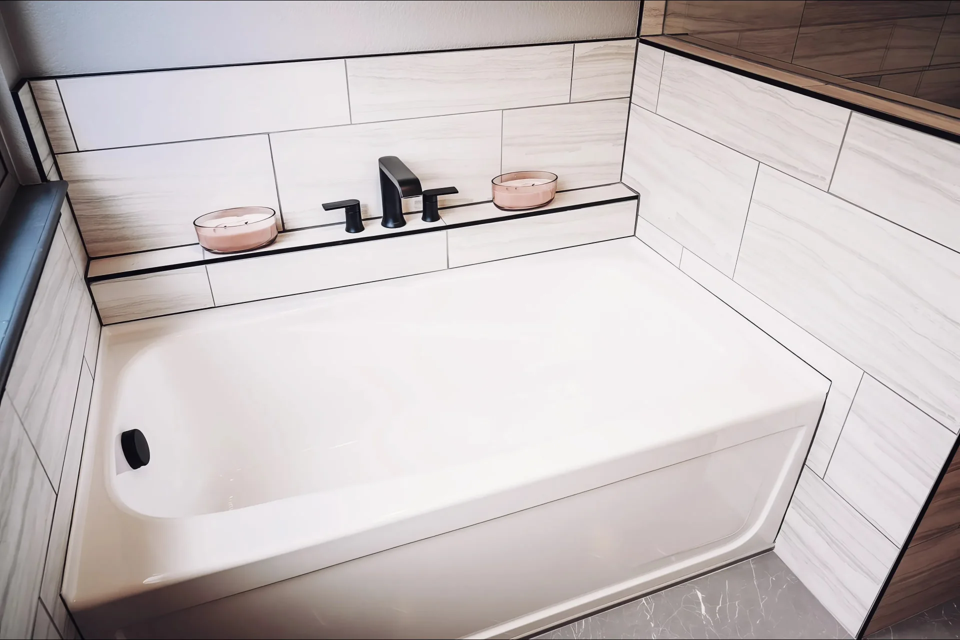 Modern white bathtub with matte black fixtures, beige tile surround, and two pink candles on the ledge, creating a relaxing ambience.