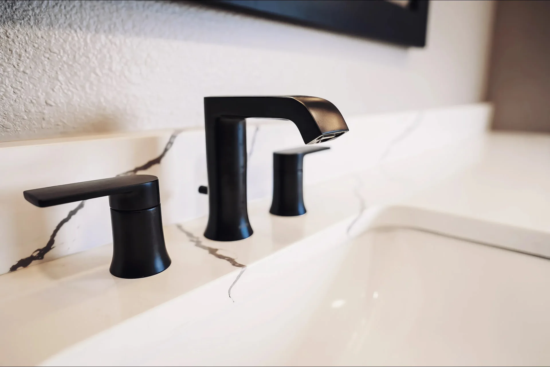 Modern bathroom sink with sleek black faucet and handles on a white marble countertop, exuding a minimalist and elegant design.