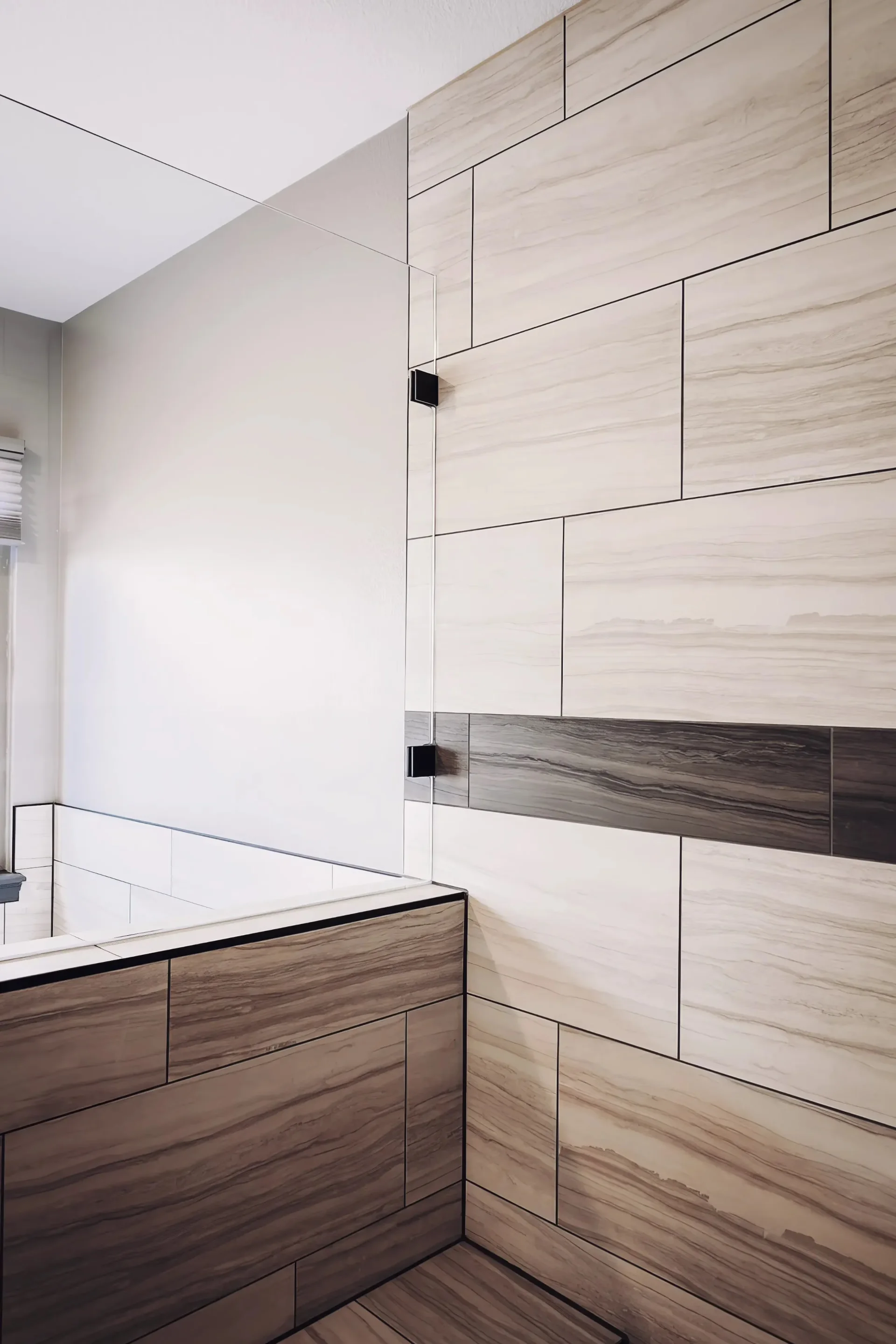 Modern bathroom with beige and gray rectangular tiles on walls and tub. Glass partition adds elegance, creating a clean and minimalistic feel.