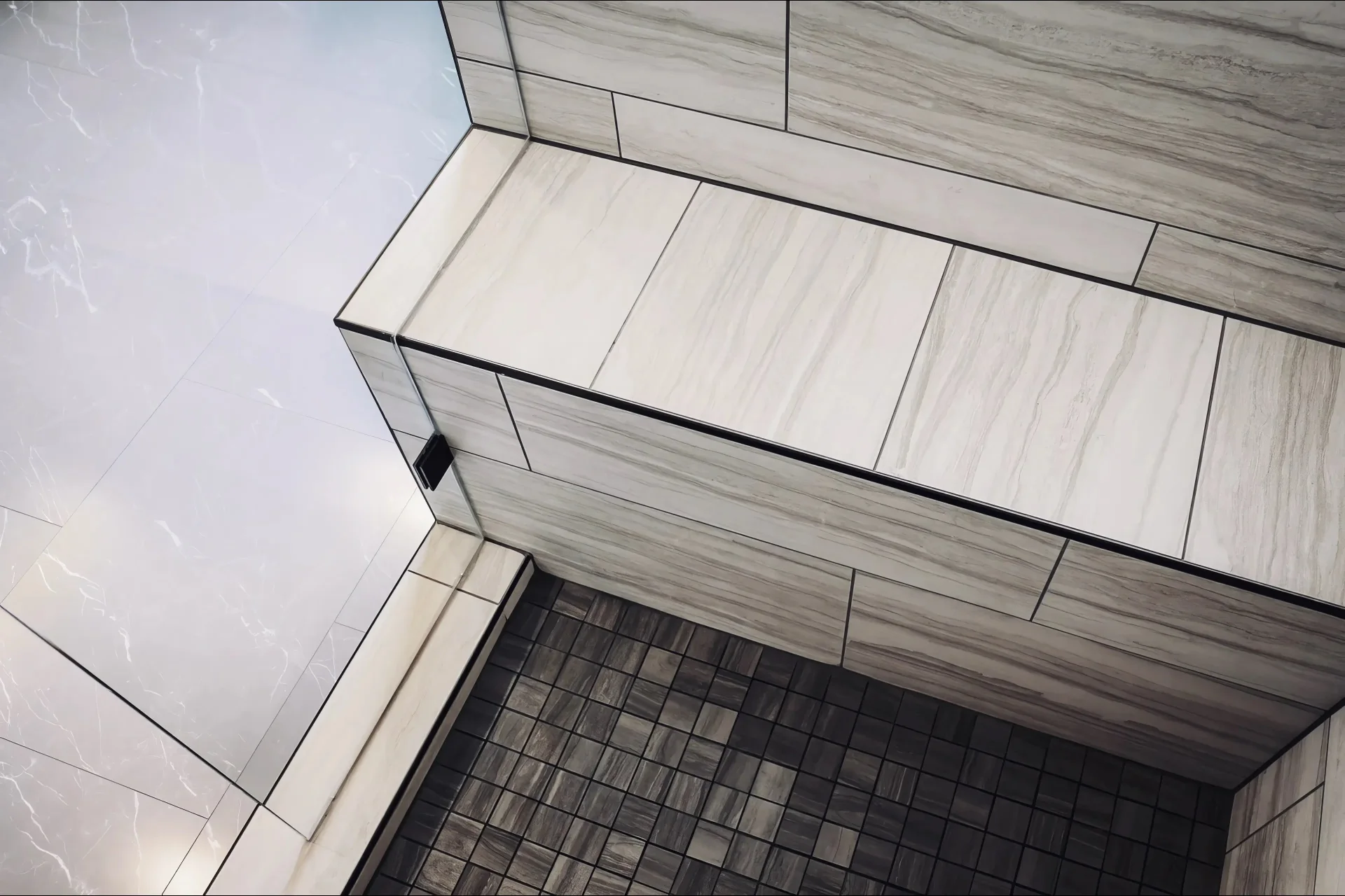 Shower bench with light gray, marble-patterned tiles, adjacent to a white tile wall. The floor has small black tiles, creating a sleek, modern look.
