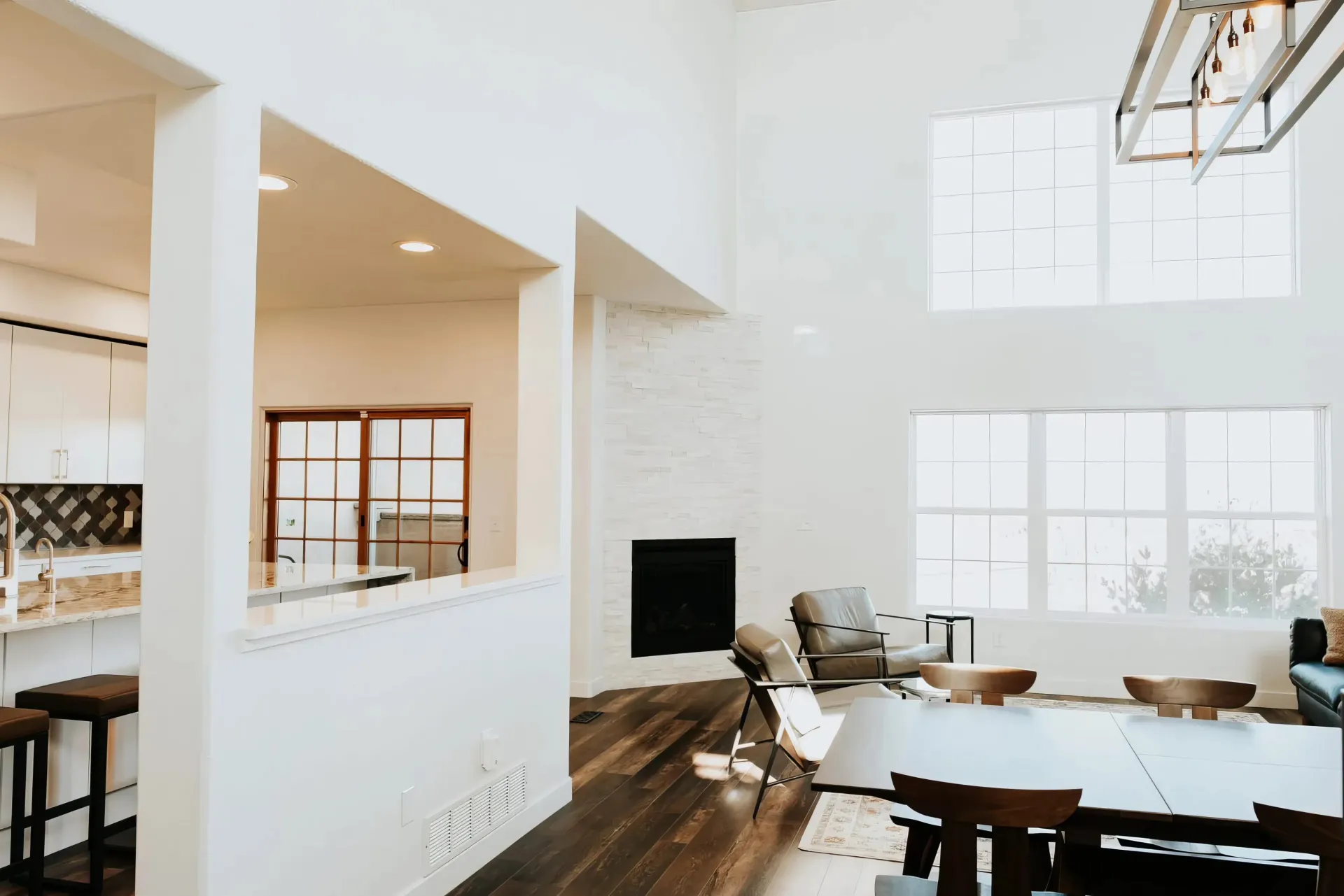 Spacious modern living room with high ceilings, large windows, and a fireplace. Warm tones from wooden floors and cozy seating create a welcoming ambiance.