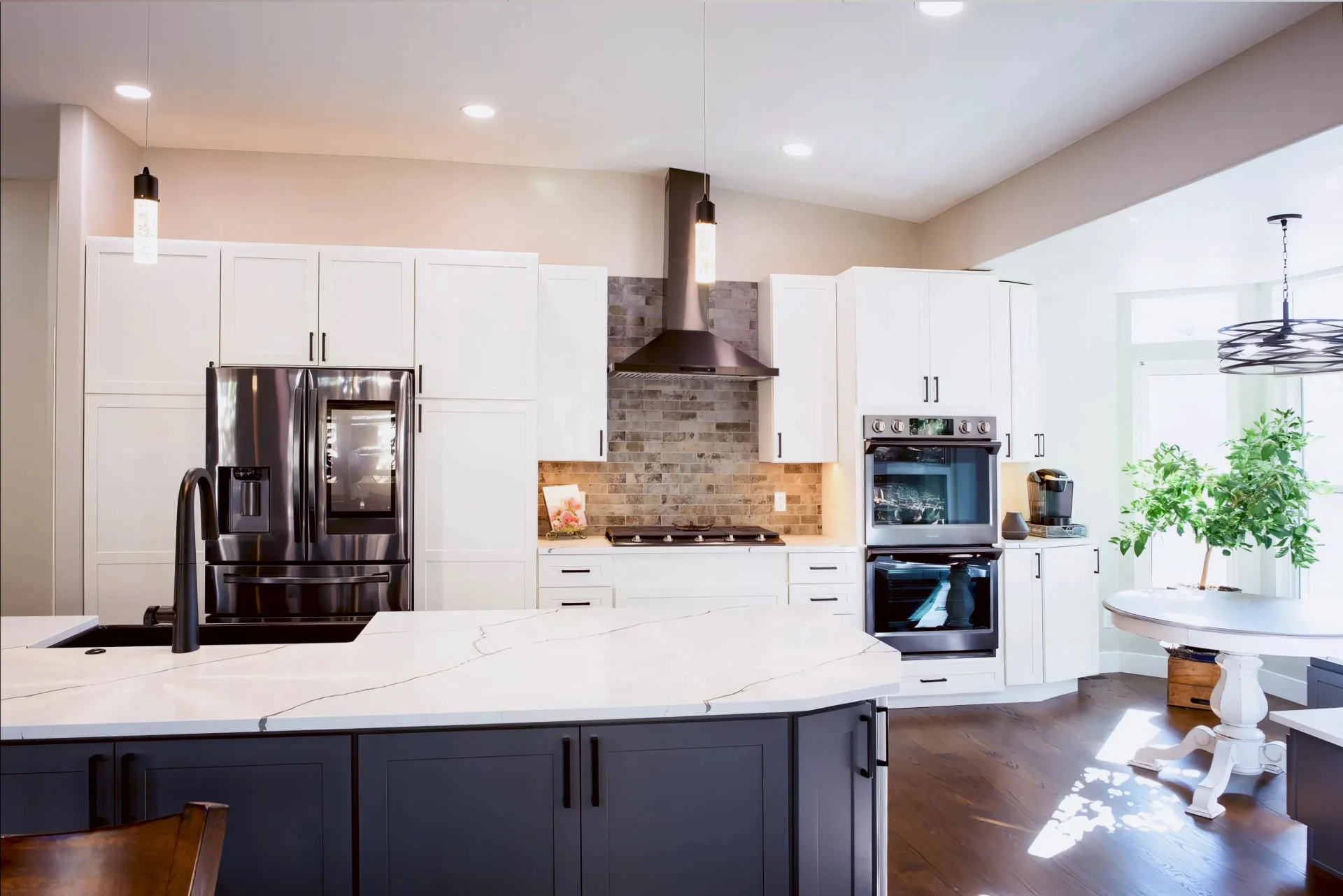 Modern kitchen with white cabinets, black appliances, and a marble island. Brick backsplash adds warmth. Bright, airy space with a cozy dining nook.