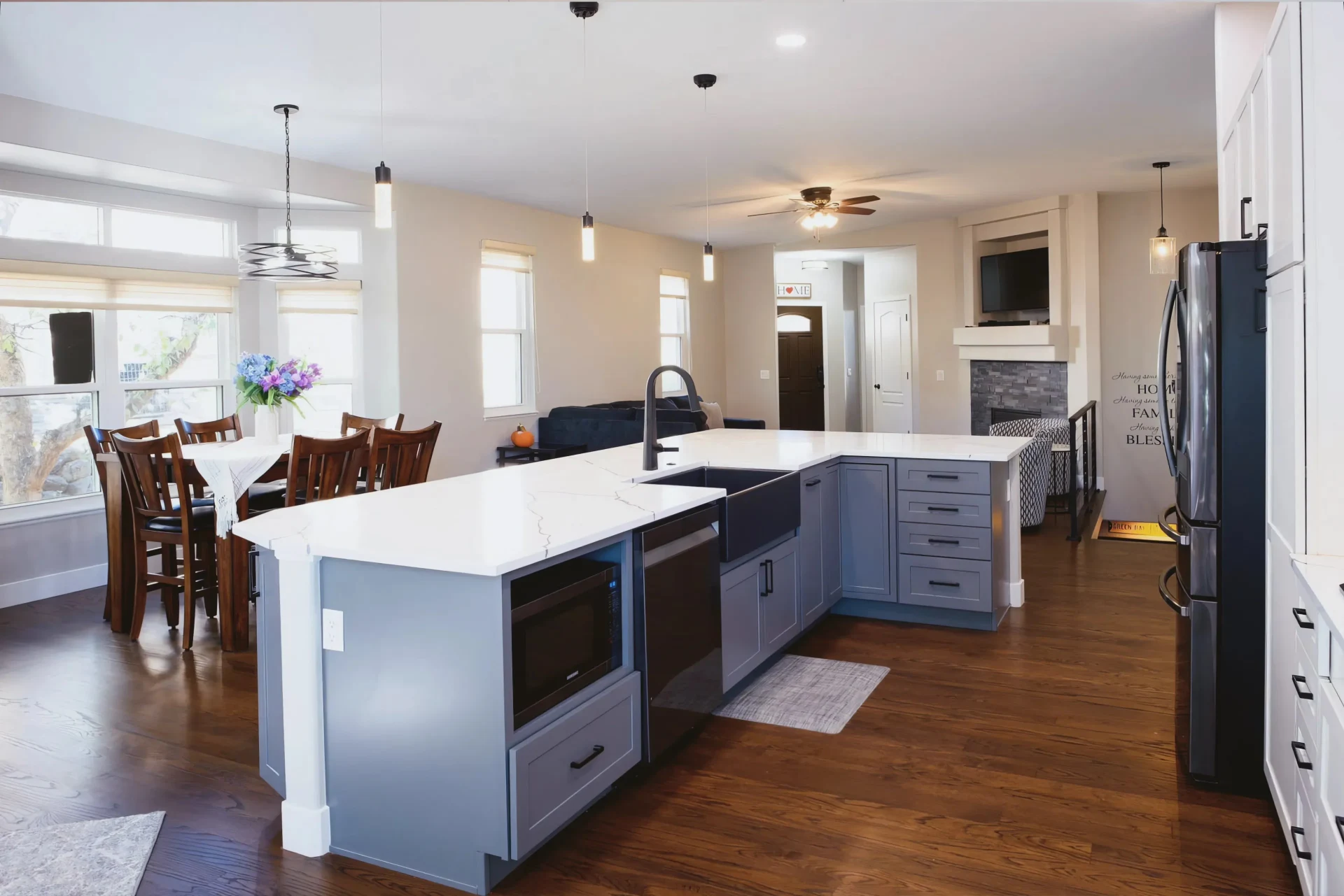 Modern kitchen with a large white island, light blue cabinets, and dark appliances. Dining table with flowers by the windows. Warm, inviting ambiance.