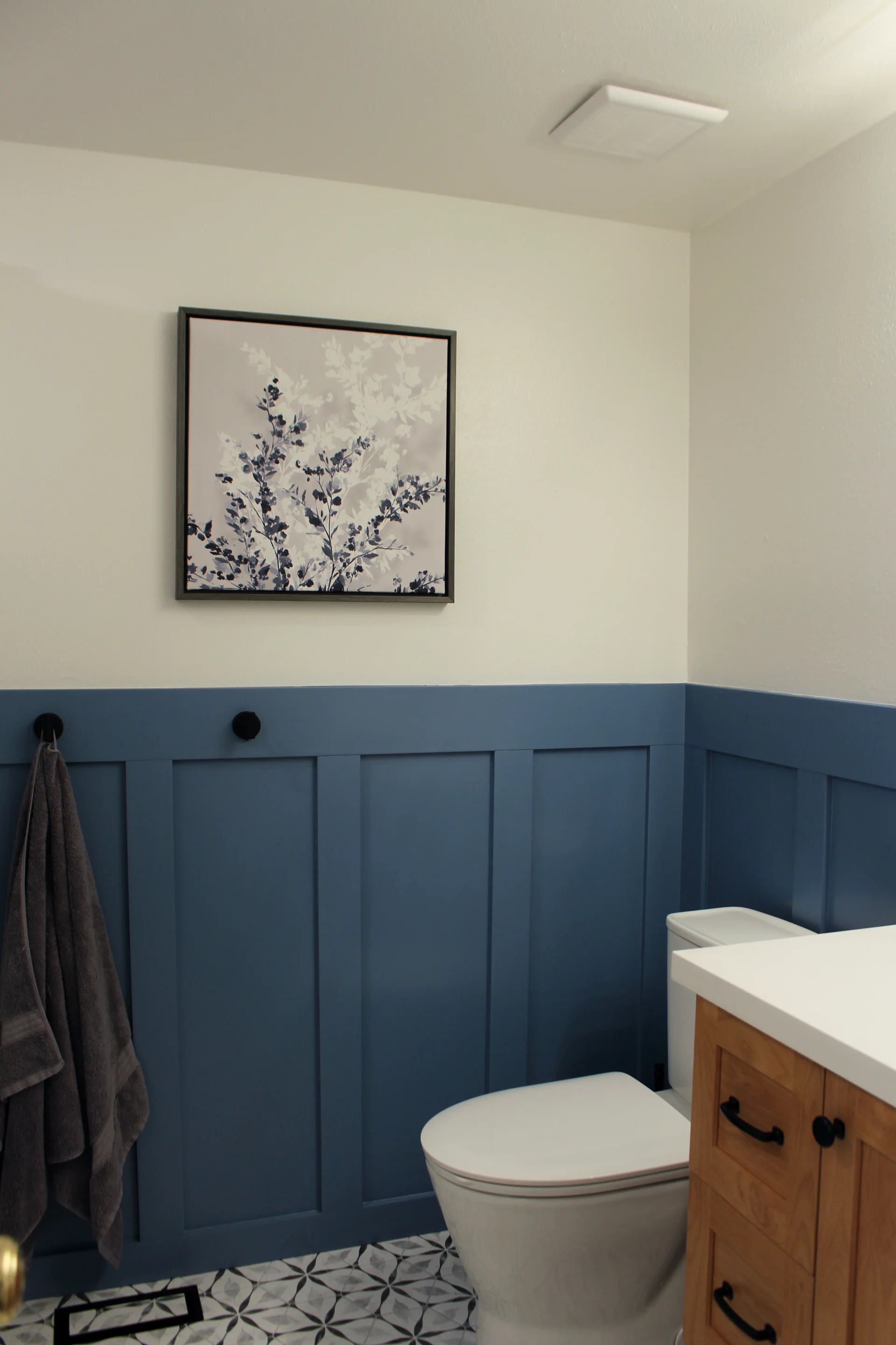 Modern bathroom with a wooden vanity, black faucet, and white countertop. A large mirror reflects a shower with a curtain, alongside blue wainscoting.