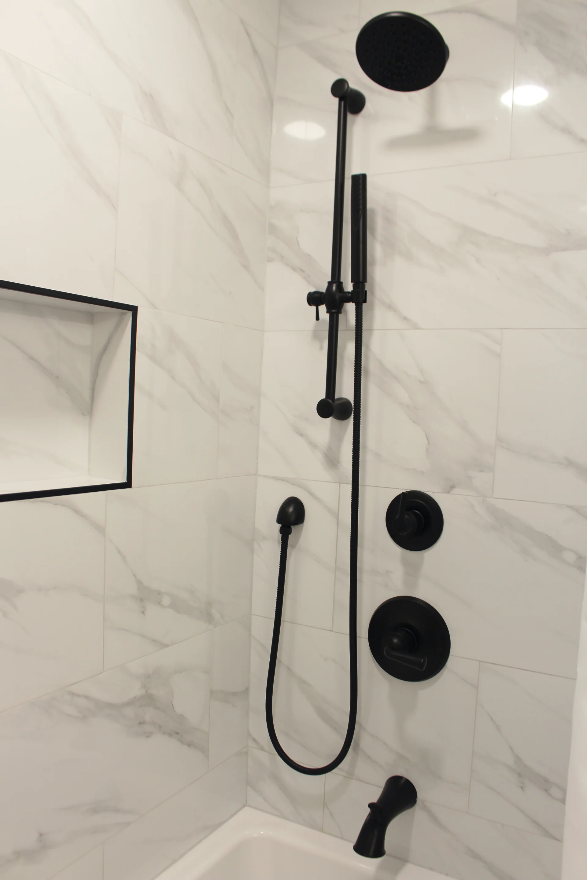 Modern shower with sleek black fixtures, including a rainfall showerhead and handheld option. Marble tiles add an elegant touch, conveying a chic, contemporary feel.