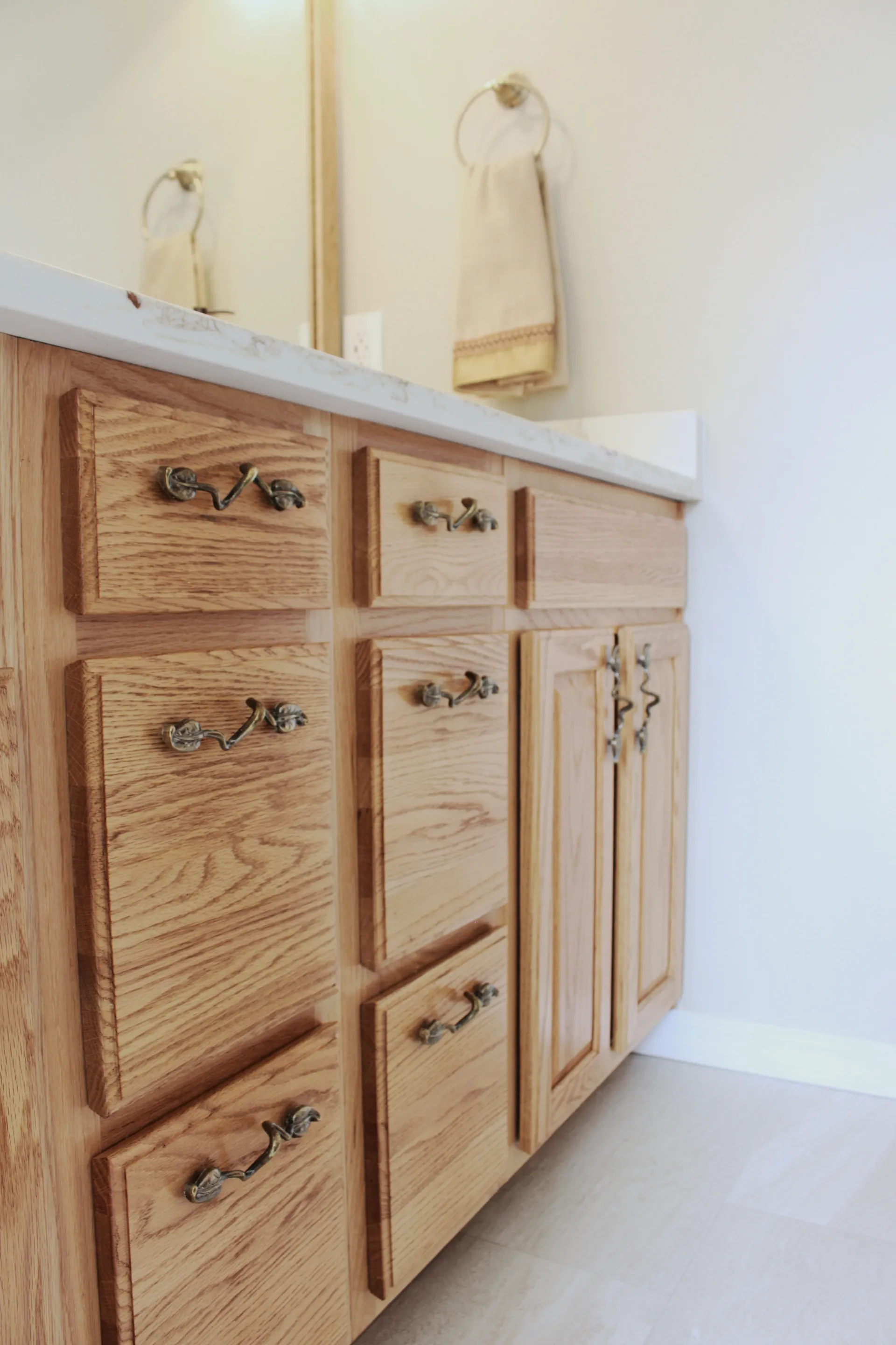 Wooden bathroom vanity with ornate handles, a white countertop, and a towel on a gold ring. The space feels warm and inviting.